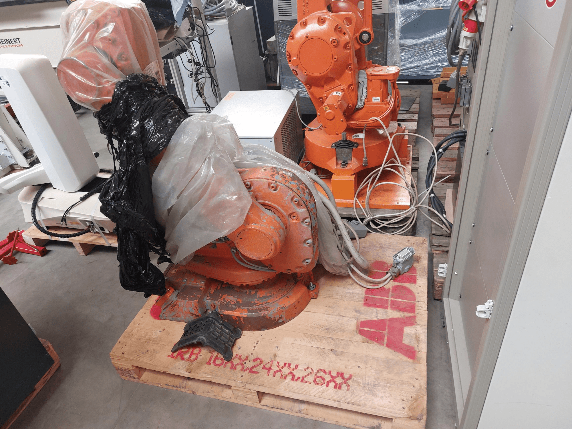 Braccio robotico ABB IRB 1600 M2004 parzialmente ricoperto di plastica, visto dal davanti, con cavi e macchinari aggiuntivi nelle vicinanze.