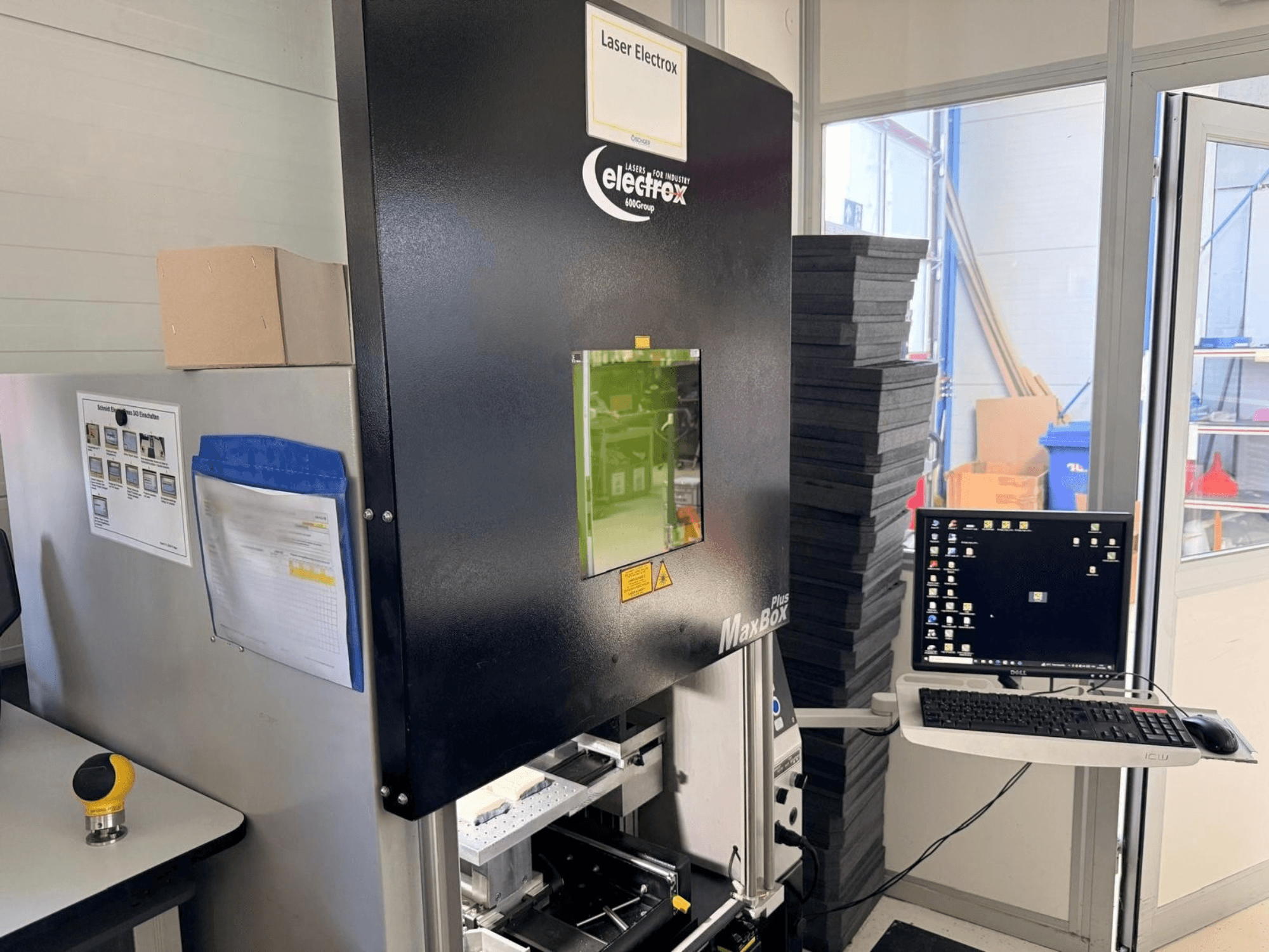 Macchina per la marcatura laser ELECTROX MaxBox Plus vista di profilo, con monitor di controllo, finestra di visualizzazione verde e area di lavoro.