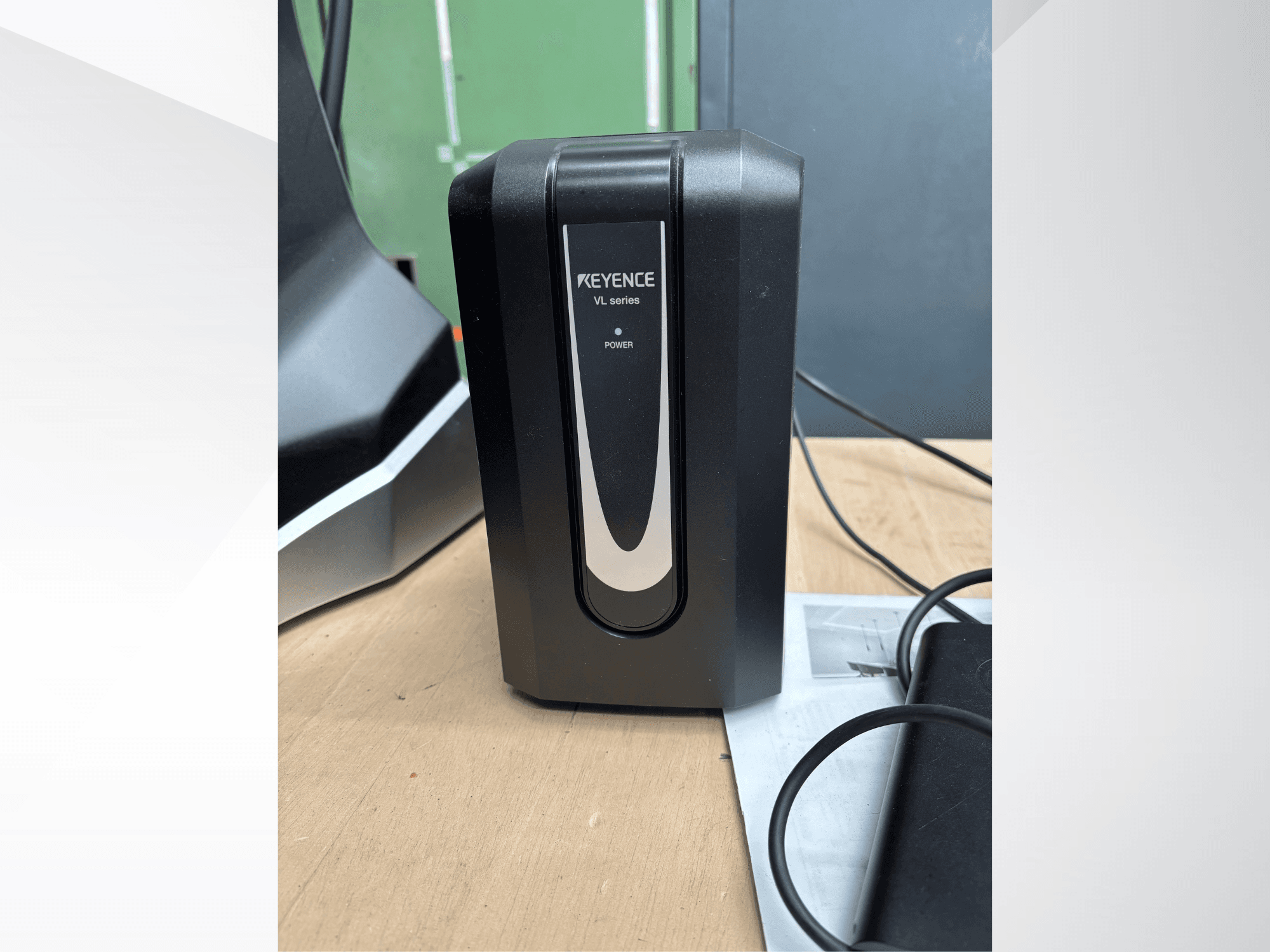 Unità di alimentazione KEYENCE serie VL nera, vista frontale, con indicatore di alimentazione e cavi collegati su una superficie in legno.