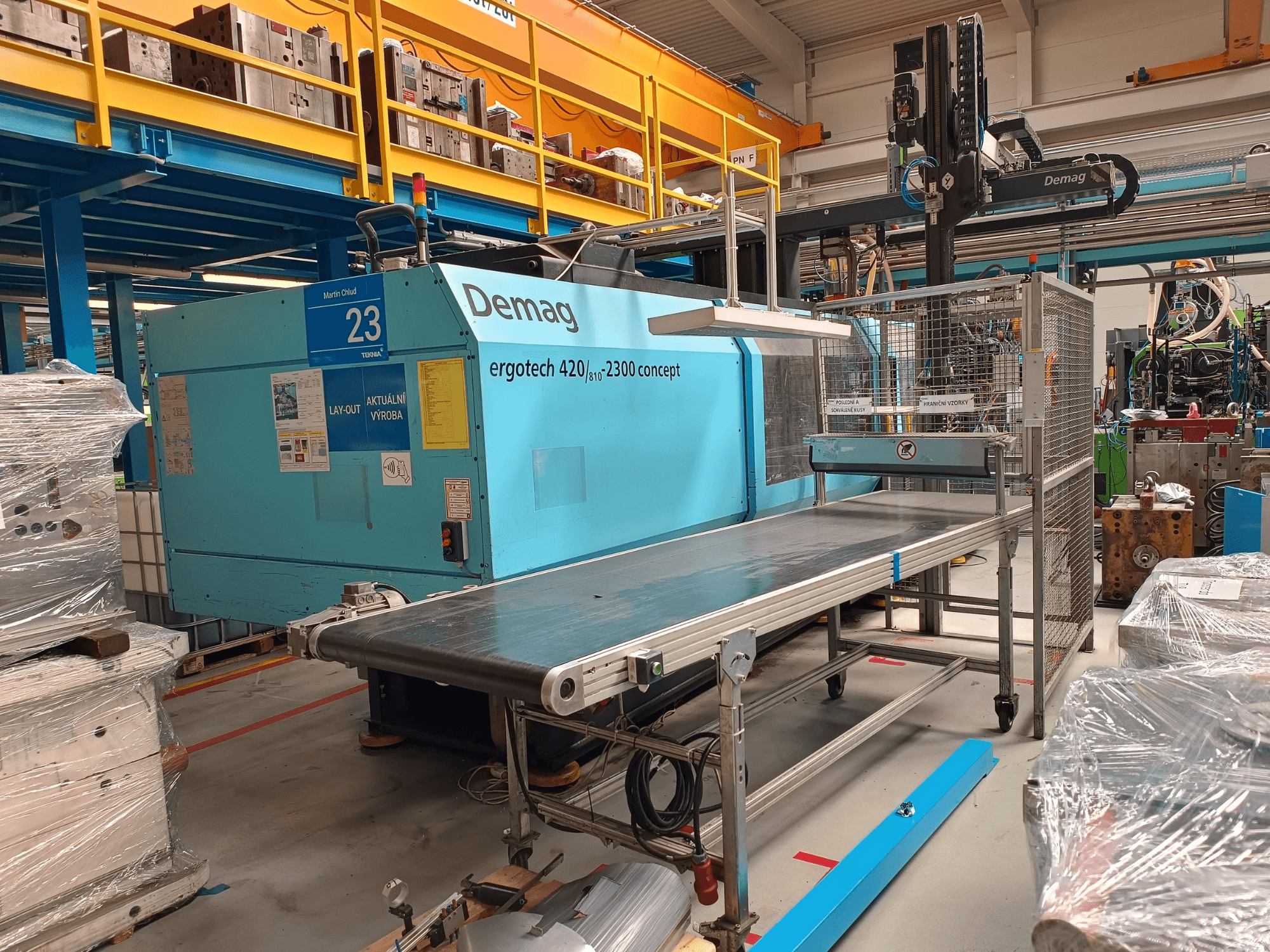 Macchina ad iniezione idraulica Demag ergotech 420/810 - 2300 in vista laterale, con convogliatore e copertura di sicurezza.