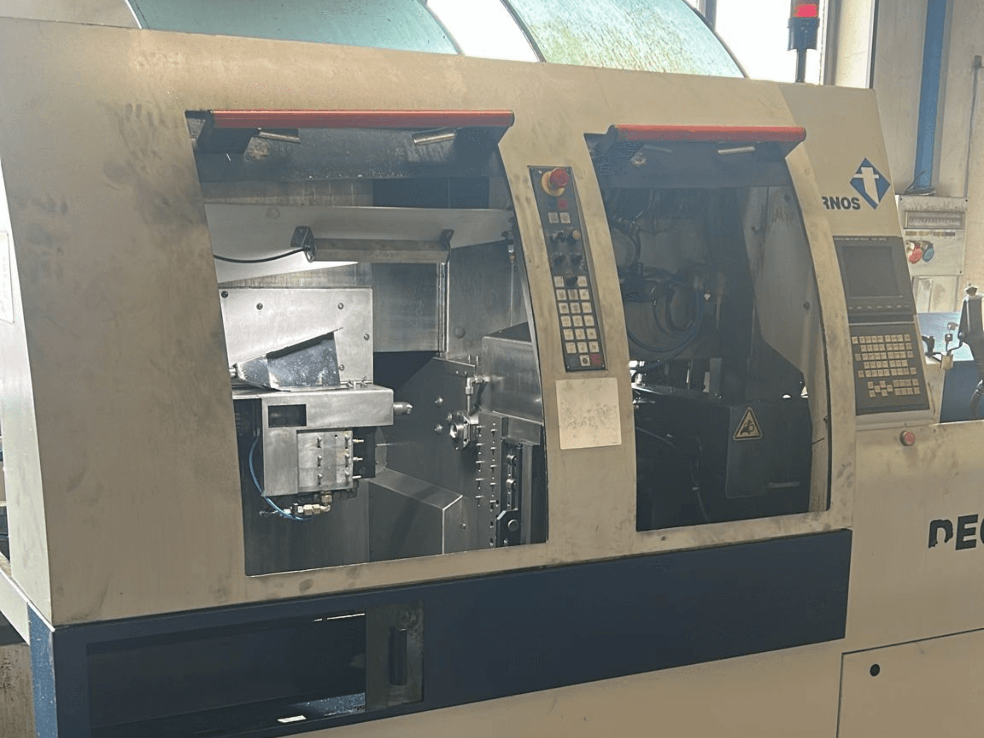 Testo Alt: Vista frontale del tornio TORNOS Deco 13 b di tipo svizzero con pannelli di controllo e componenti interni visibili.