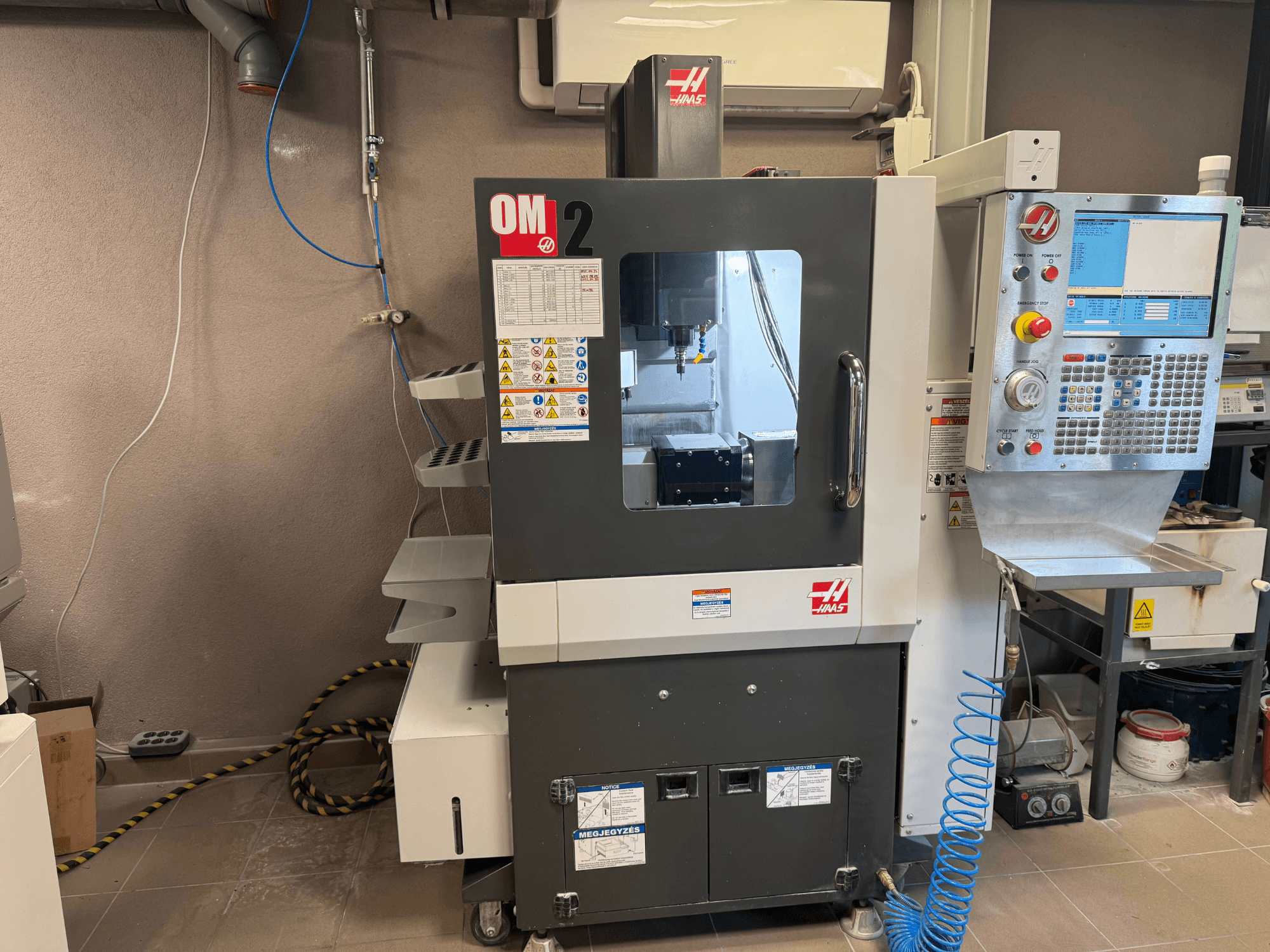 Macchina CNC Haas OM-2, vista frontale, con pannello di controllo, mandrino ed etichette di sicurezza, in un ambiente di officina.