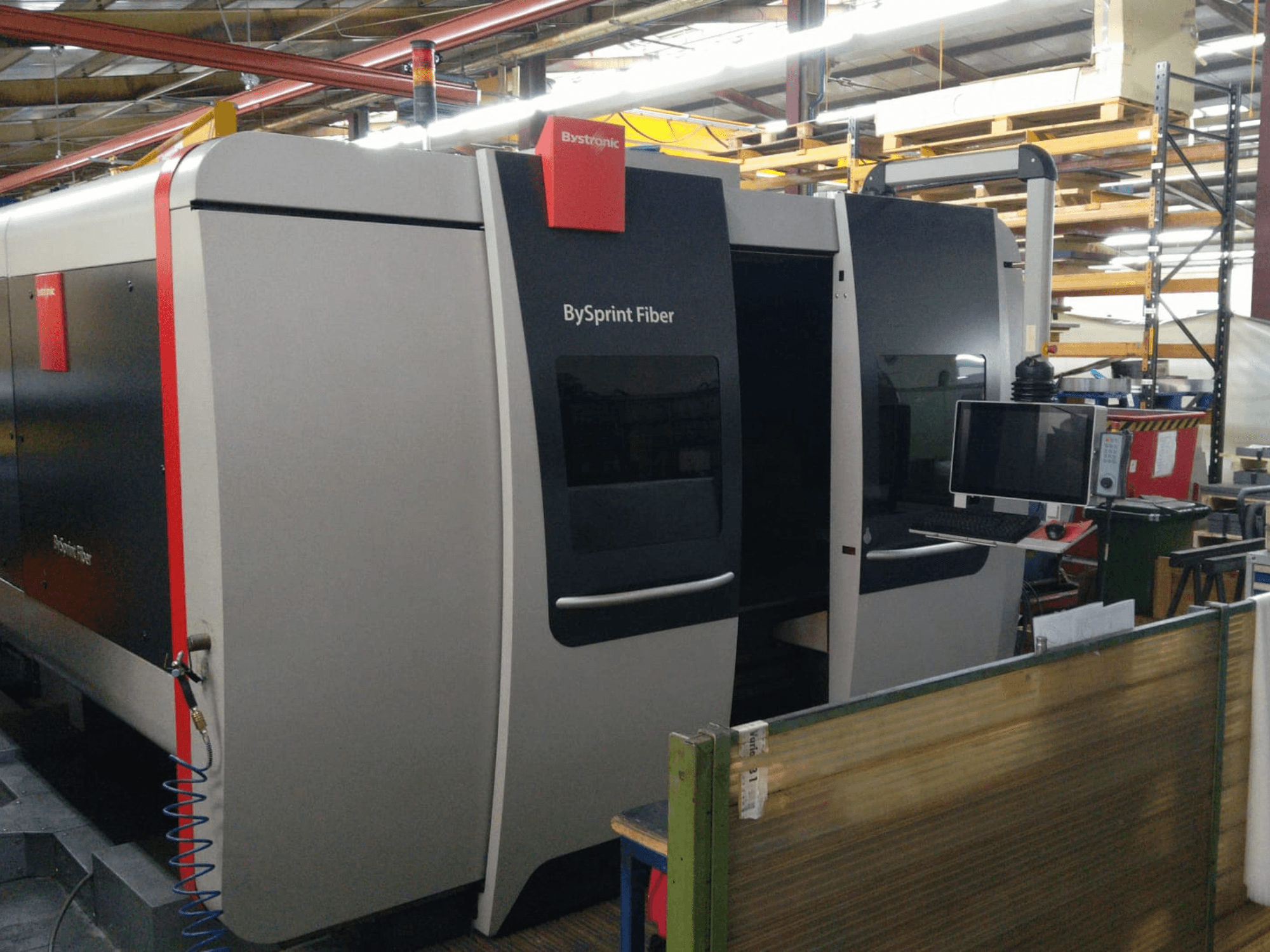 Taglierina laser in fibra Bystronic BySprint, vista frontale con pannello di controllo; i dettagli visibili includono due porte e un monitor sul lato.
