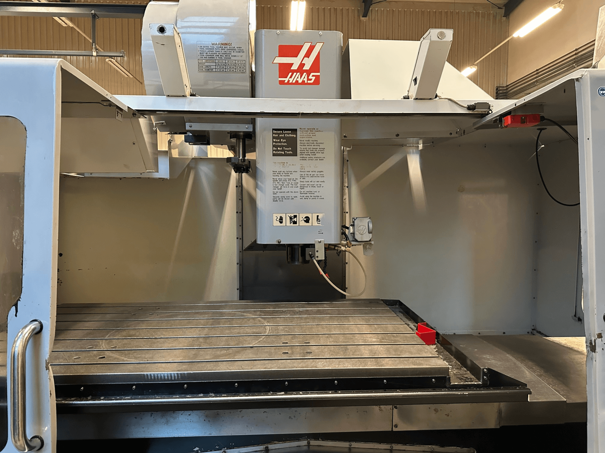 Fresatrice CNC Haas, modello VF-2, vista frontale che mostra i comandi, il piano di lavoro in metallo e l'etichetta di sicurezza sul pannello.