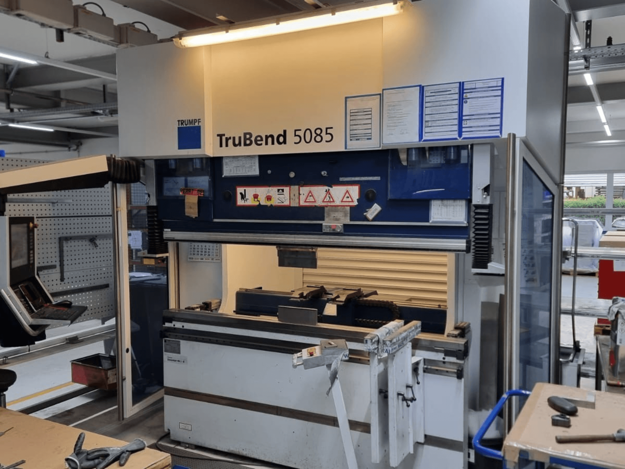 Curvatrice TRUMPF TruBend 5085, vista frontale, con pannello di controllo, stazione operativa e avvertenze di sicurezza all'interno dell'officina.