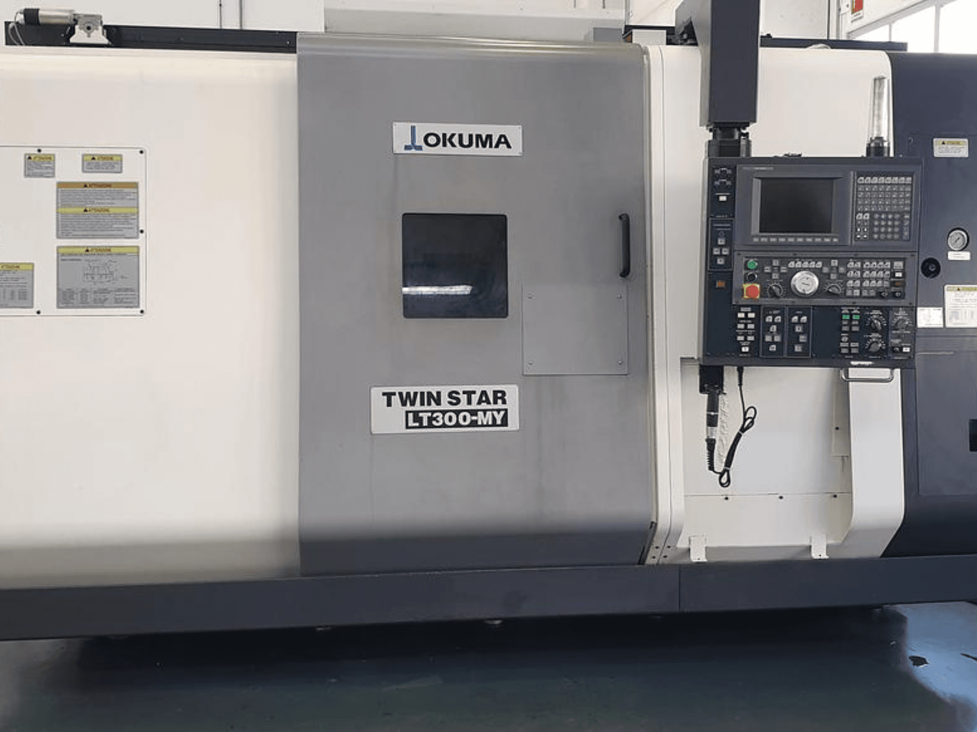Tornio CNC Okuma Twin Star LT300-MY in vista laterale, con pannello di controllo, pulsanti operativi ed etichette di sicurezza.