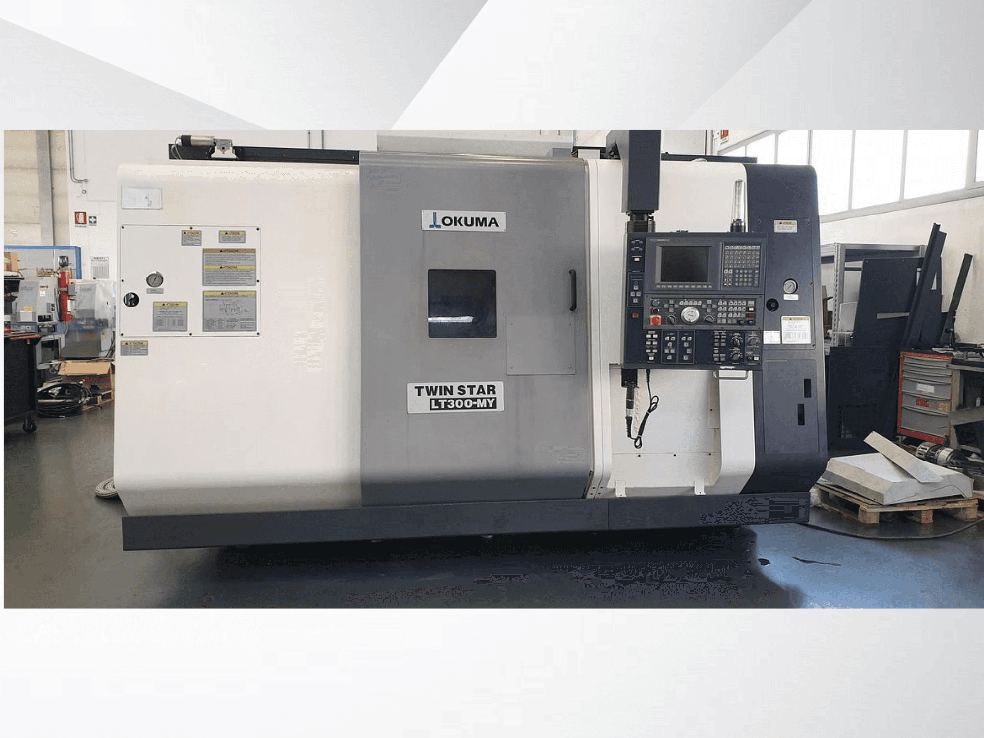Tornio CNC Okuma Twin Star LT300-MY, vista frontale con pannello di controllo ed etichette operative visibili.