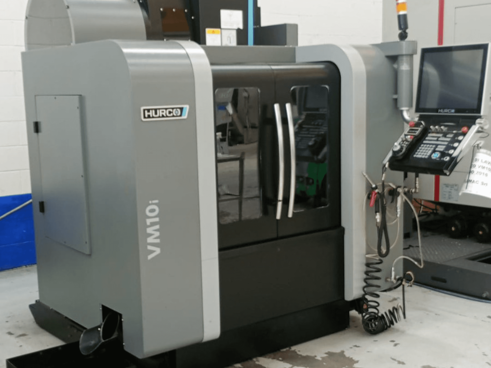 Centro di lavorazione verticale Hurco VM10i visto di lato, con doppia porta, pannello di controllo e cavi visibili necessari per il funzionamento.