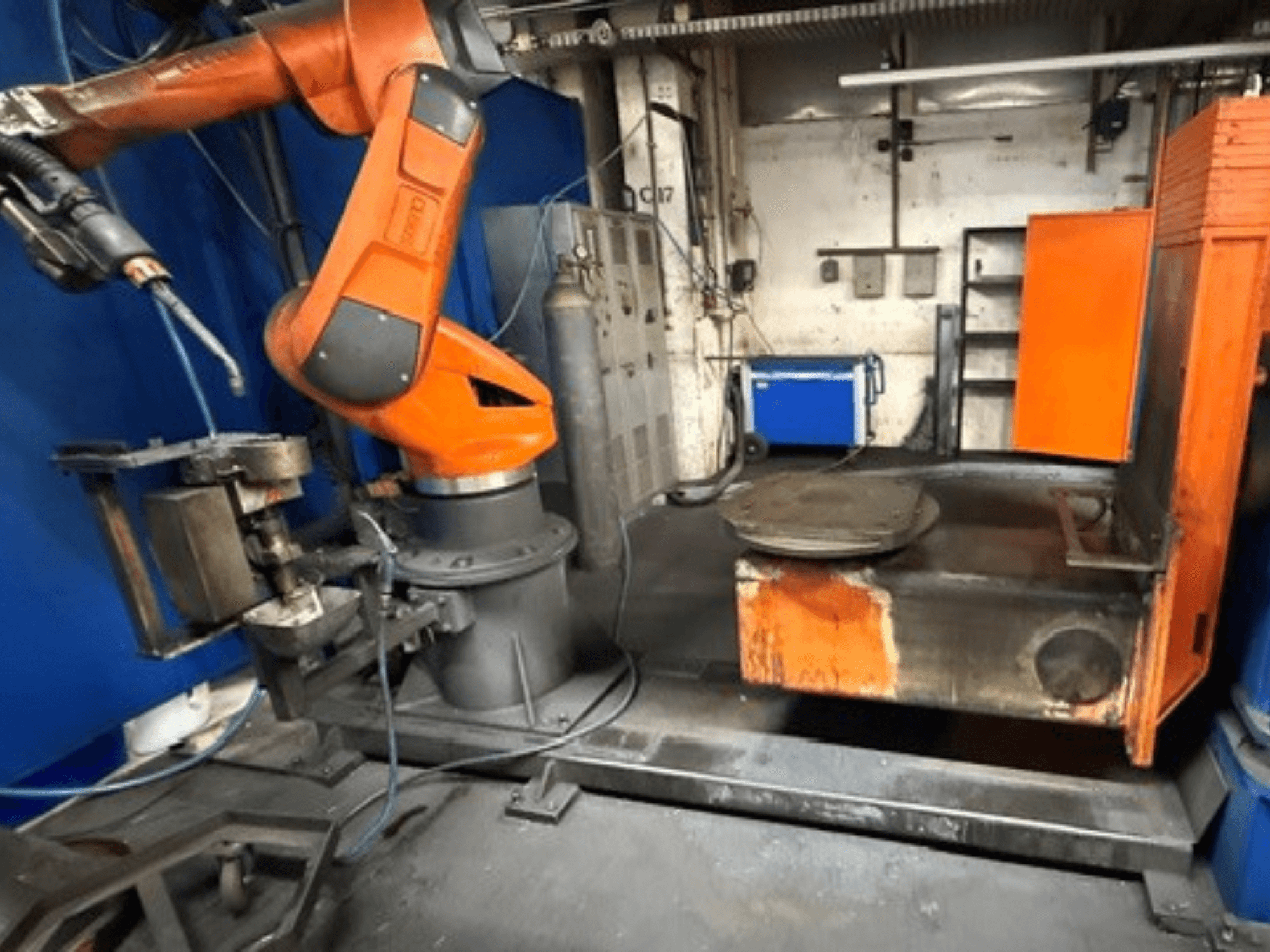 Robot di saldatura CLOOS C50 visto di fronte, con braccio robotico arancione e piano di lavoro in metallo.
