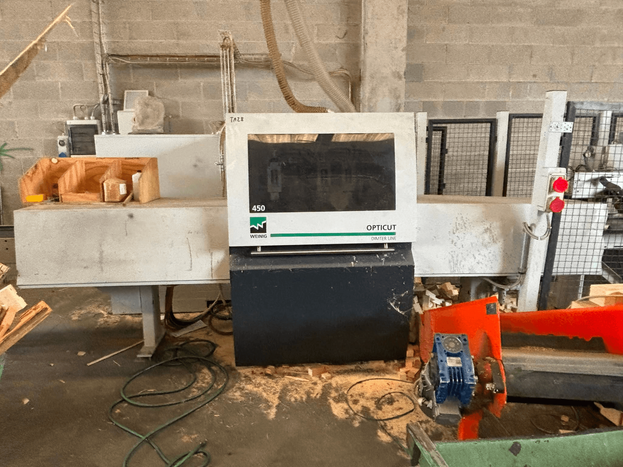 Sega trasversale ottimizzante WEINIG OptiCut 450, vista frontale, con pannello di controllo, area di taglio e pezzi di legno sul tavolo.