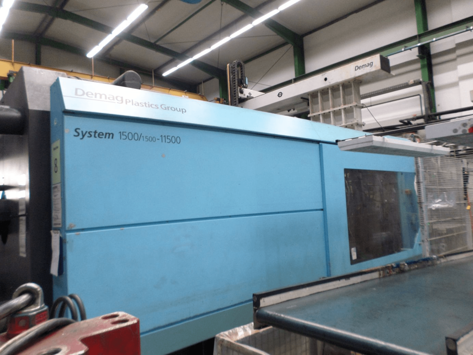 Macchina per lo stampaggio a iniezione idraulica Demag D 650 di colore blu, vista laterale che mostra l'etichetta "System 1500/1500-11500" e l'area operativa.