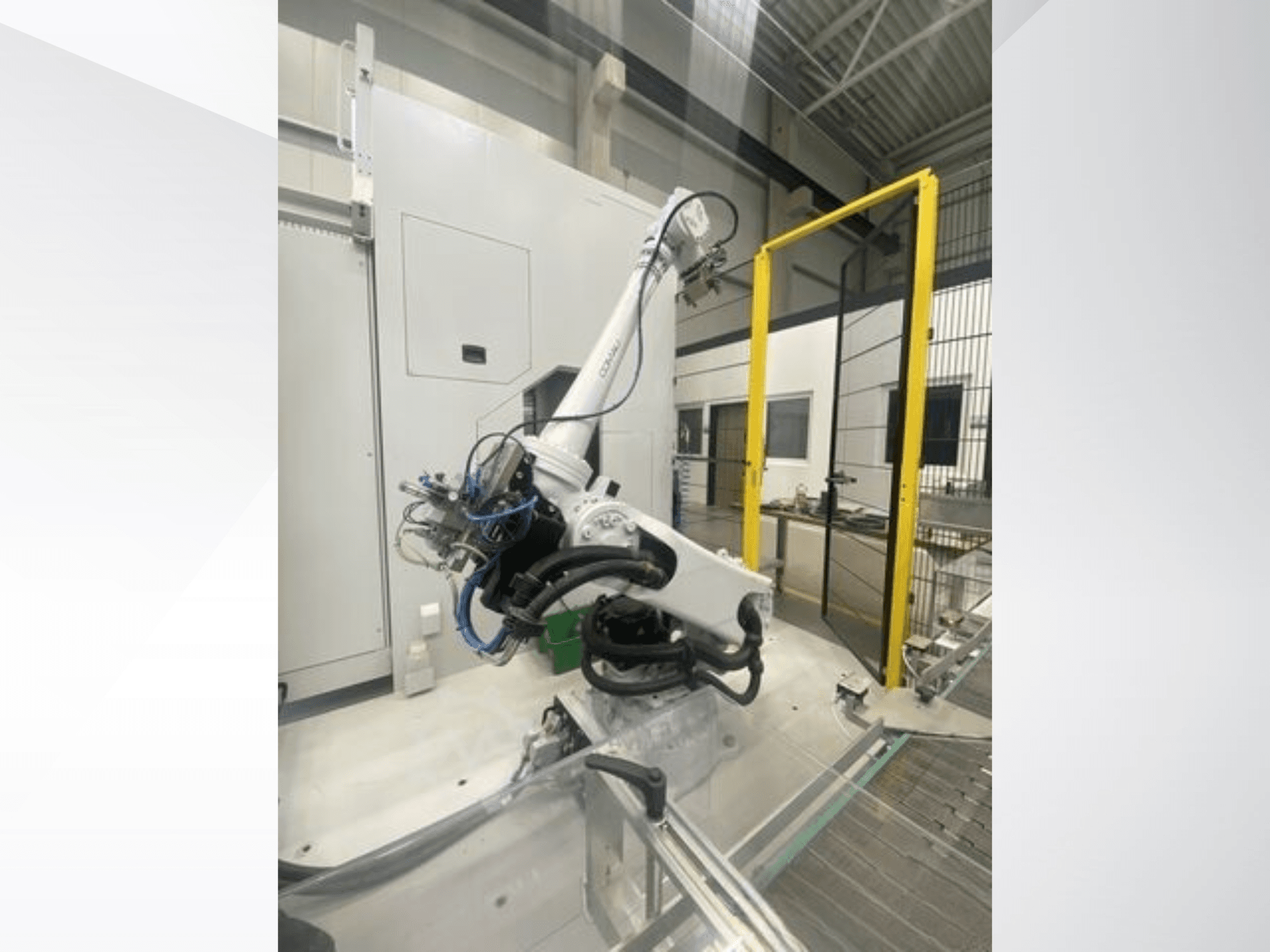 Braccio robotico COMAU Smart NJ 40-2.5 in vista laterale, con cavi e cancello di sicurezza giallo in un ambiente di fabbrica.