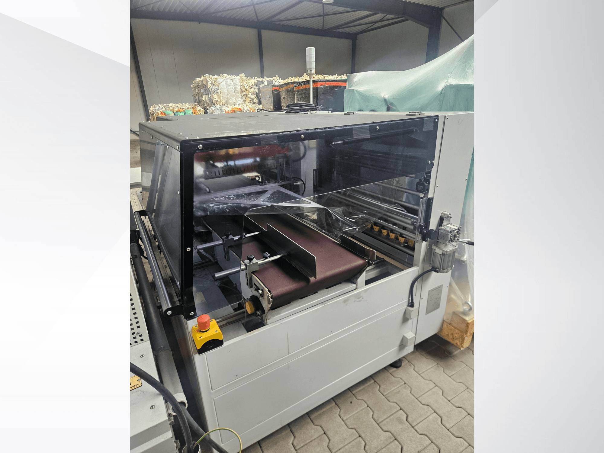 Macchina AMTEC Speed Shrink 40 PRO, vista frontale, che mostra un meccanismo di lavorazione della plastica dotato di una copertura di sicurezza trasparente e di un nastro trasportatore.