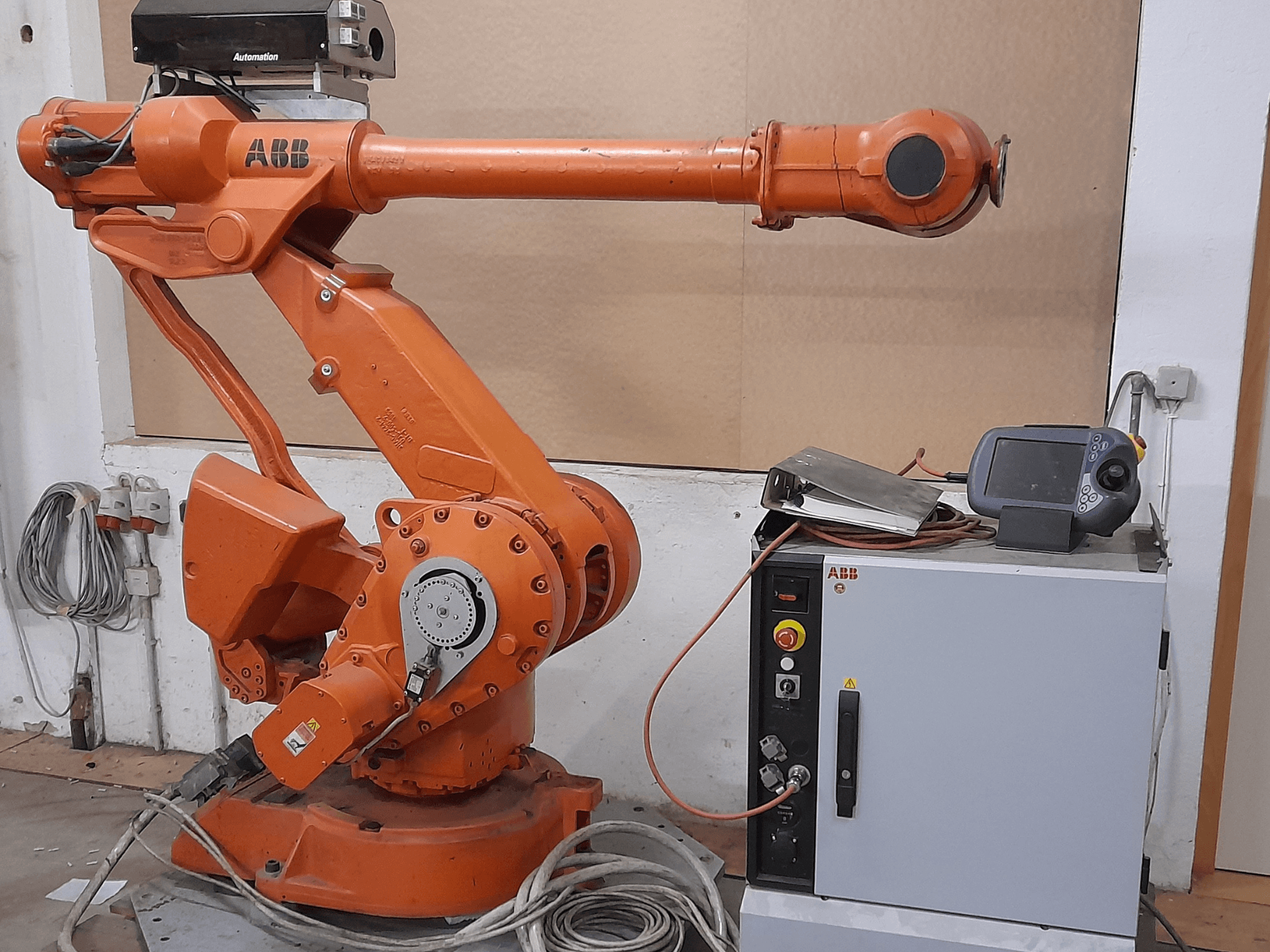 Braccio robotico ABB arancione con pannello di controllo, vista frontale, che mostra cavi e apparecchiature di automazione.