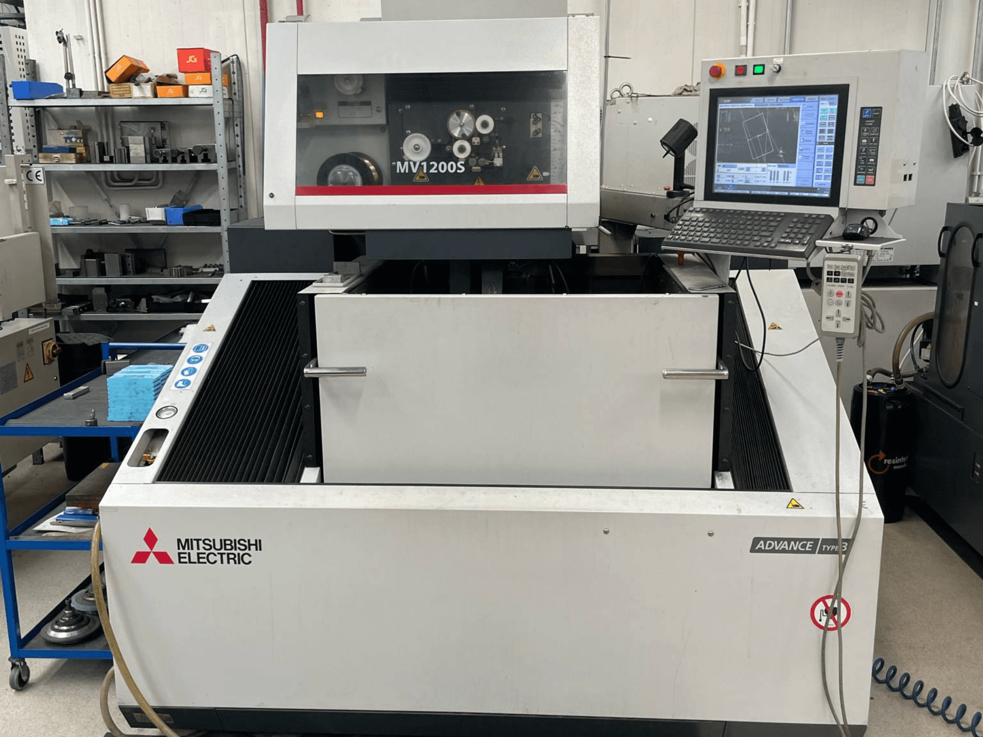 Macchina per elettroerosione a filo Mitsubishi MV1200S vista frontale, con pannello di controllo e area di lavoro, con le avvertenze di sicurezza ben visibili.