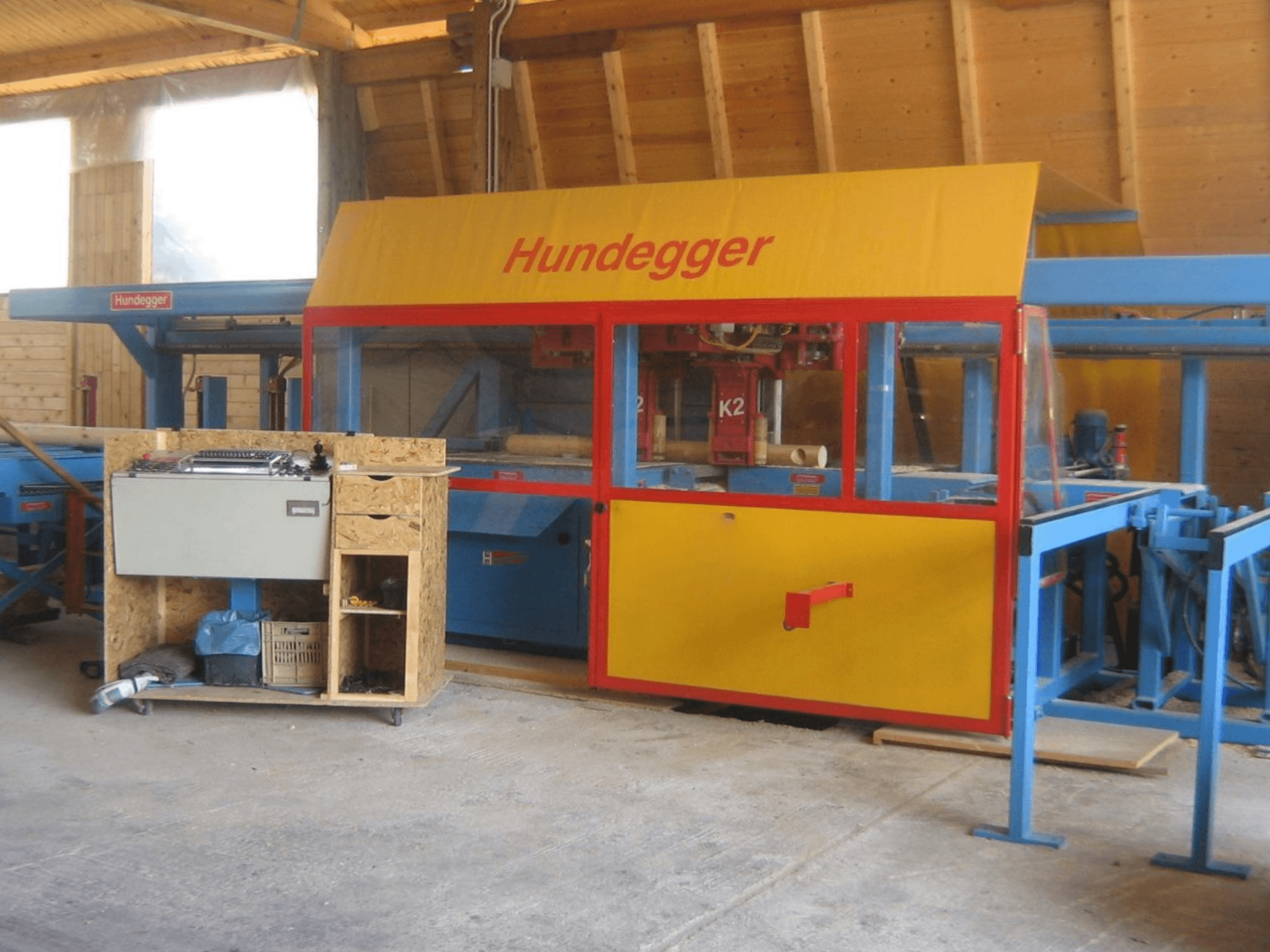 Centro di lavorazione del legno CNC HUNDEGGER K2 4 assi in un'officina, vista frontale che mostra il design giallo e blu con il piano di lavoro.