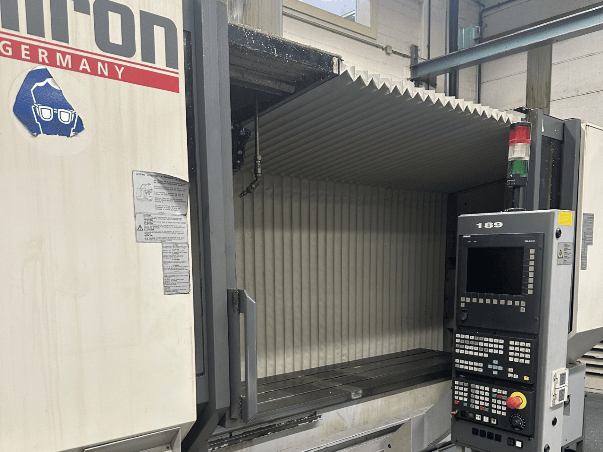 Testo Alt: Vista frontale di una macchina CNC Hermle con un pannello di controllo che mostra i pulsanti e il display, con un'area di lavoro aperta.