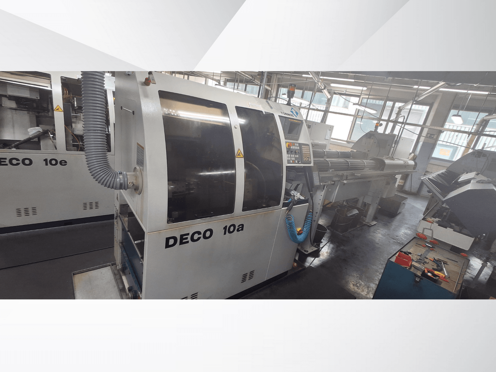 Macchina DECO 10a CNC in officina, con vista frontale, pannello di controllo e sistema di scarico. Struttura robusta e strumenti di precisione.