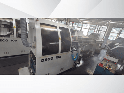Macchina DECO 10a CNC in officina, con vista frontale, pannello di controllo e sistema di scarico. Struttura robusta e strumenti di precisione.