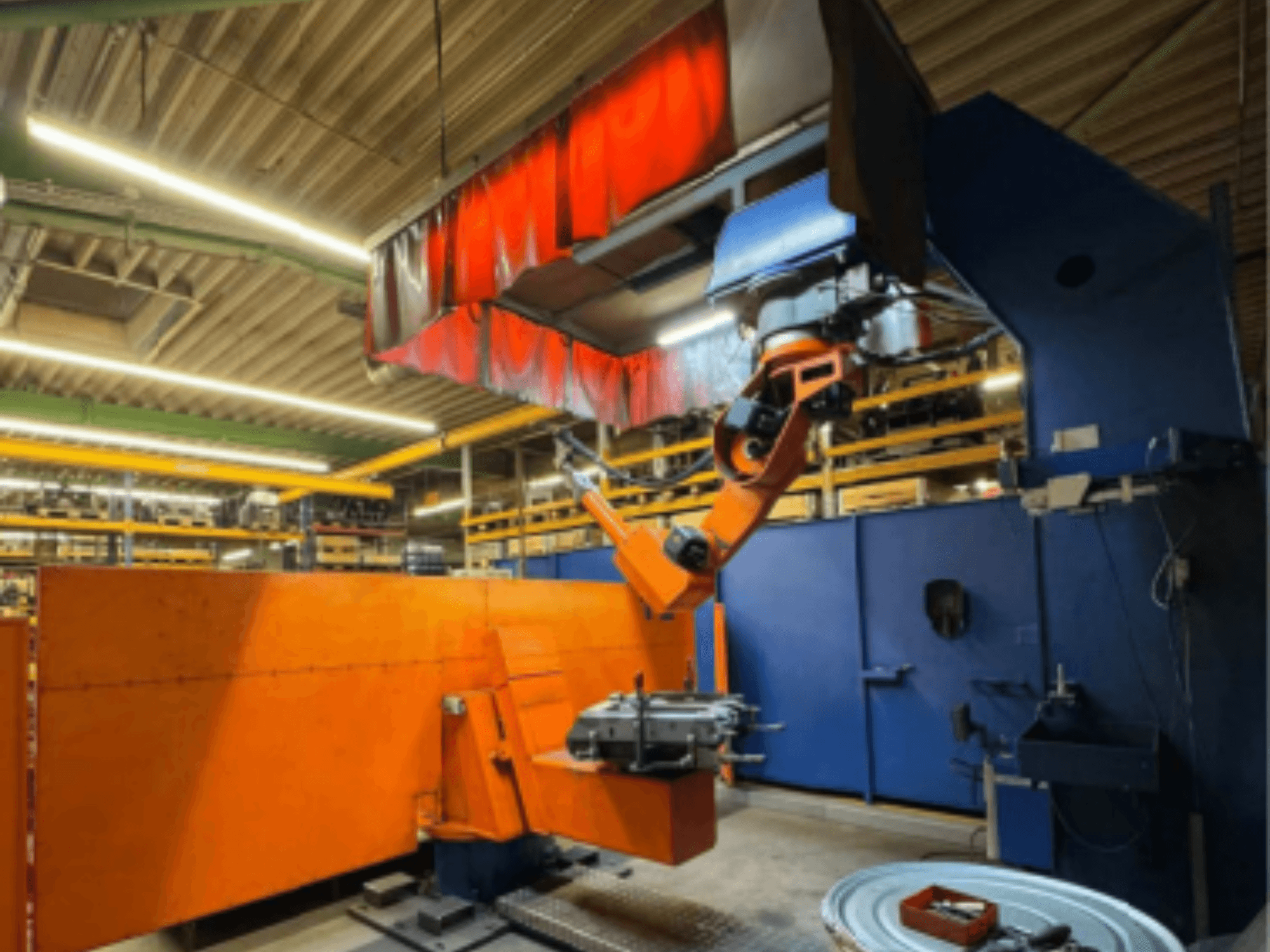 Robot di saldatura CLOOS Romat 350 e in un ambiente industriale, vista frontale con braccio arancione che tiene un pezzo in lavorazione sotto una tenda aerea.