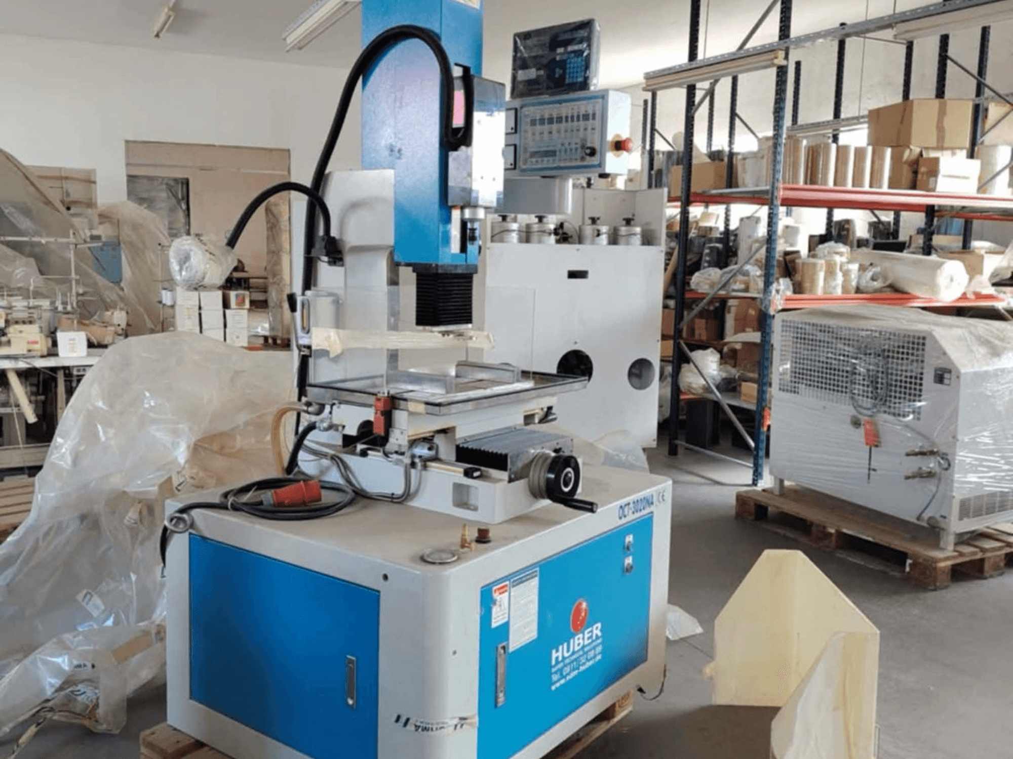 Macchina per elettroerosione a tuffo HUBER OCT-3020 NA in un'officina, vista frontale che mostra l'involucro blu e grigio, i comandi digitali e l'area di lavoro.