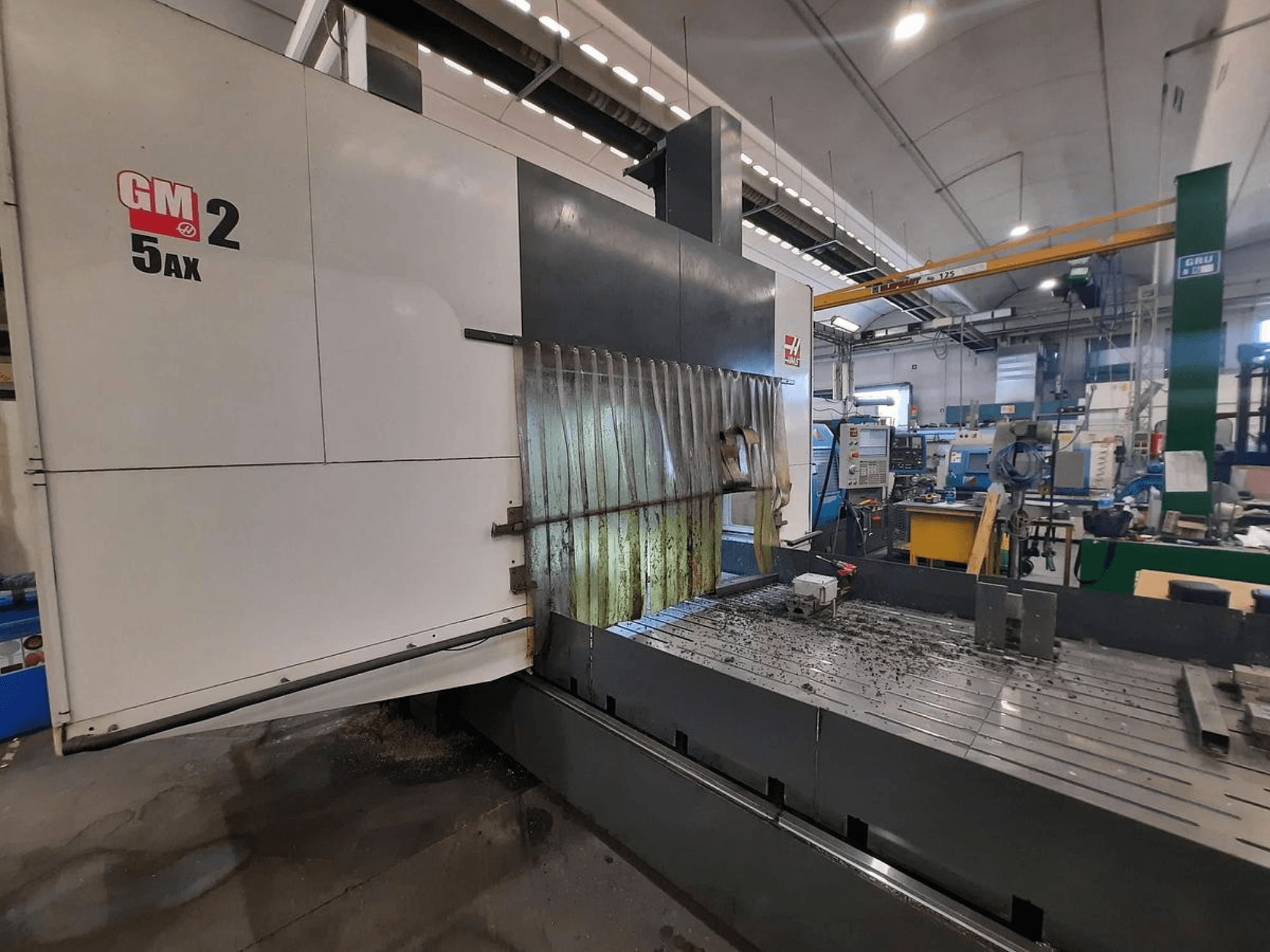 Macchina CNC GM 2 5AX in un'officina, vista laterale, che mostra l'area operativa e i trucioli di metallo sulla superficie del banco.