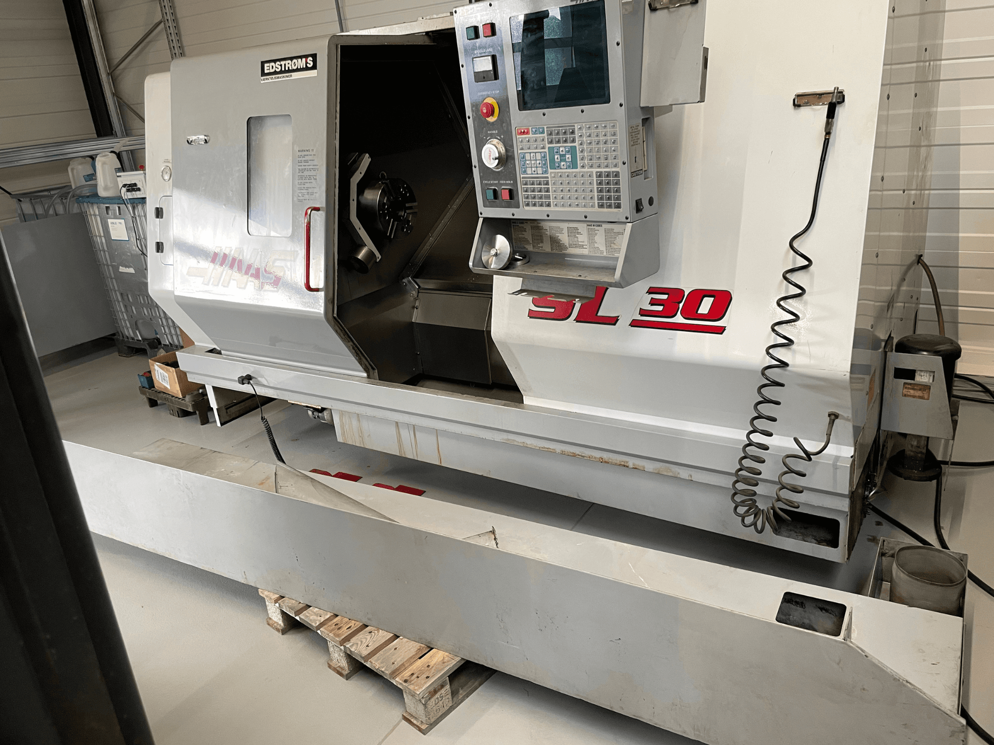 Tornio CNC Haas SL 30 in officina, vista laterale, con pannello di controllo e mandrino aperto per la lavorazione.