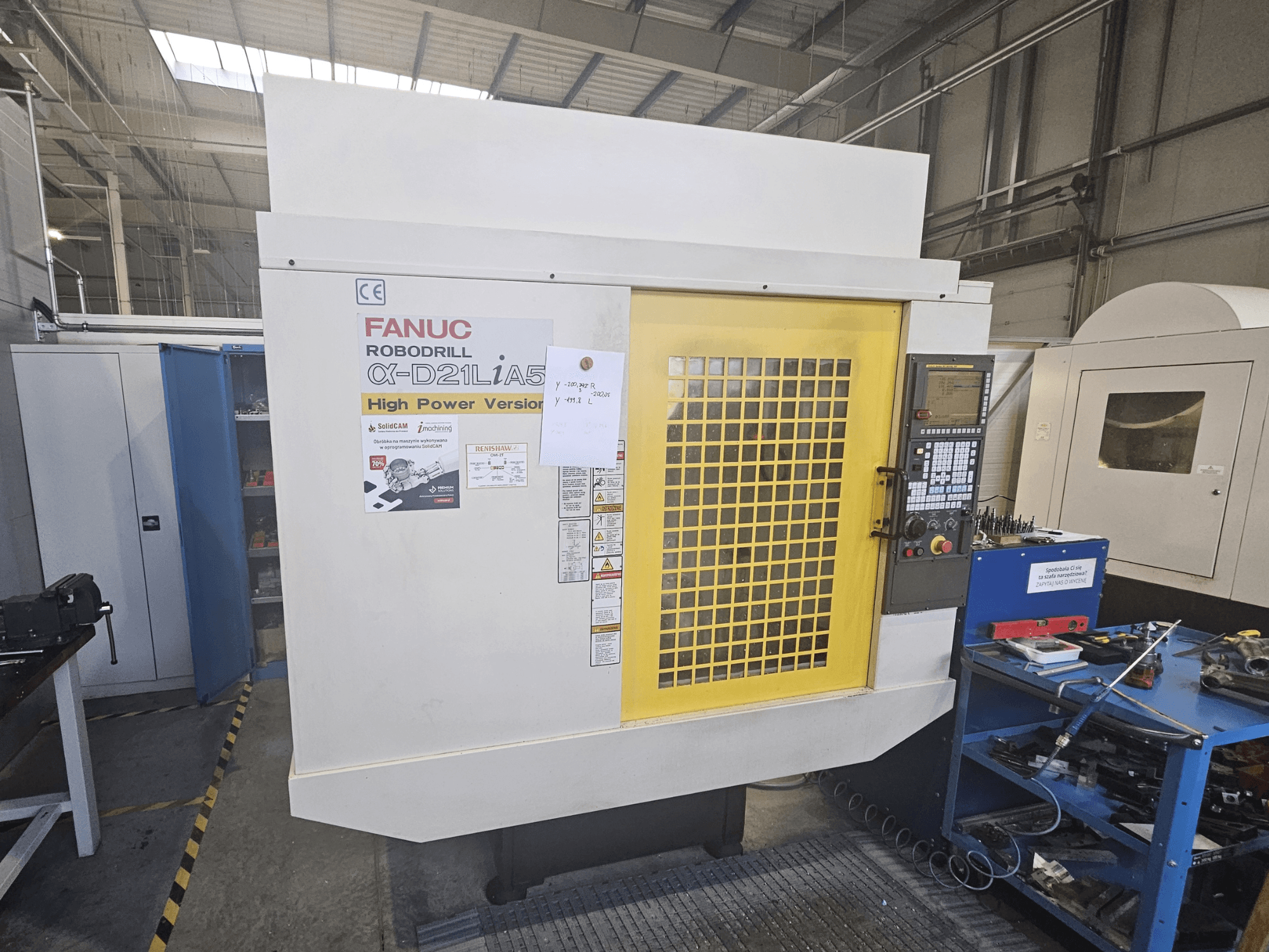 Vista frontale di un FANUC Robodrill α-D21LiA5 con lo sportello di sicurezza giallo, il pannello di controllo e gli strumenti di lavoro nelle vicinanze.