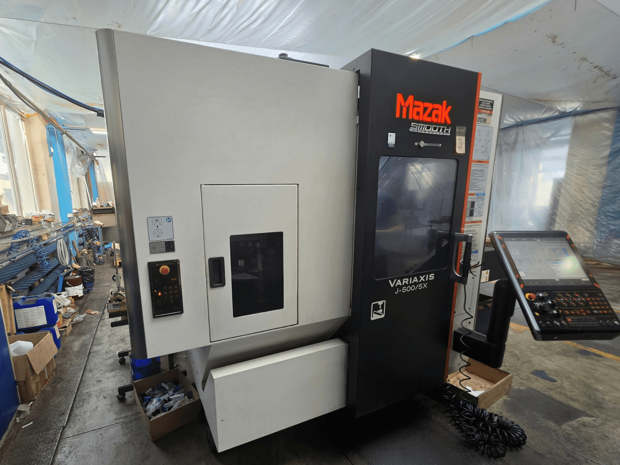 Centro di lavorazione verticale Mazak VARIAXIS J-500/5X, vista laterale che mostra i comandi e il display, collocato in un ambiente di officina.
