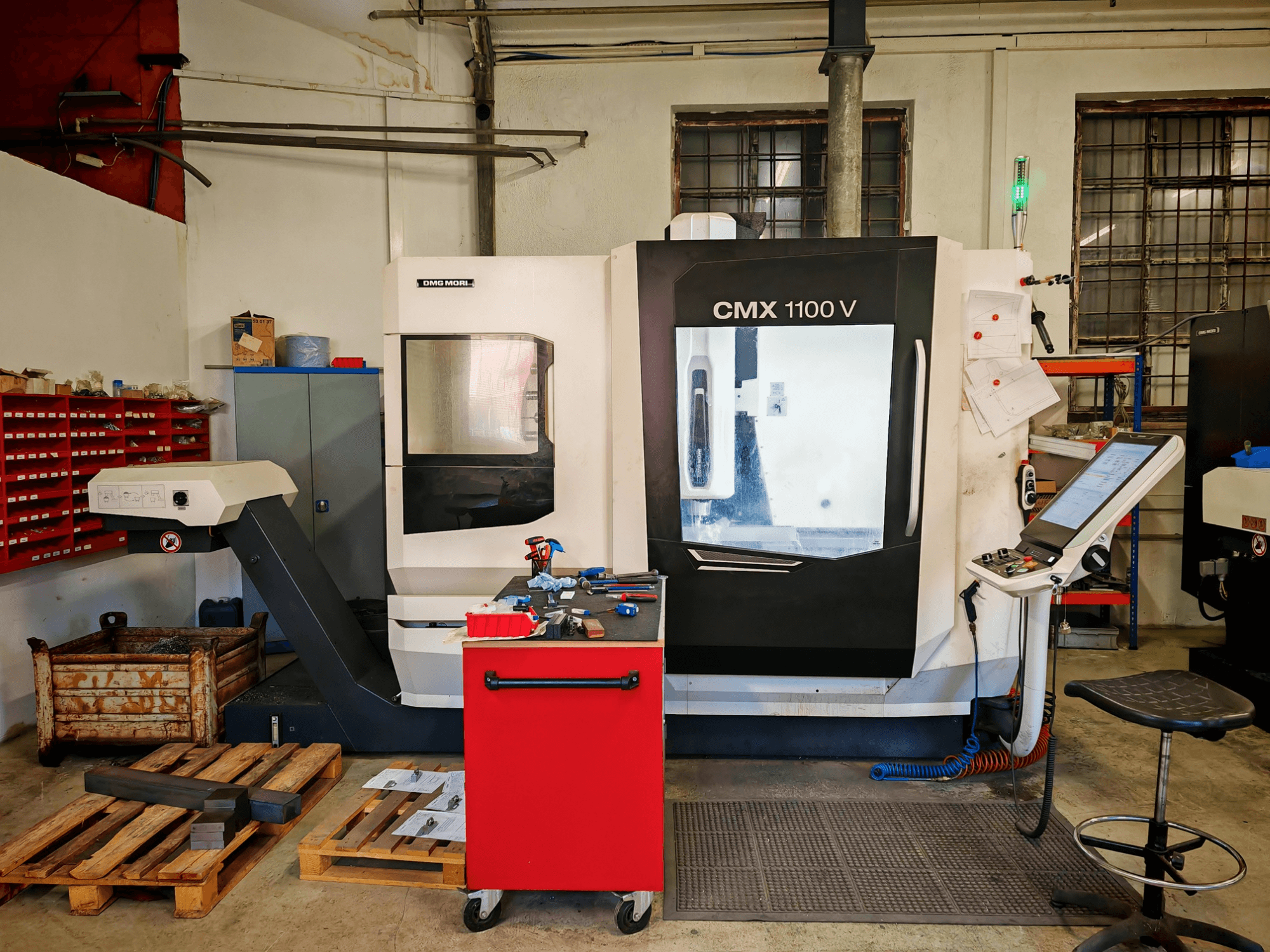 Centro di lavorazione verticale DMG MORI CMX 1100 V in officina, vista frontale, con pannello di controllo e utensili circostanti.