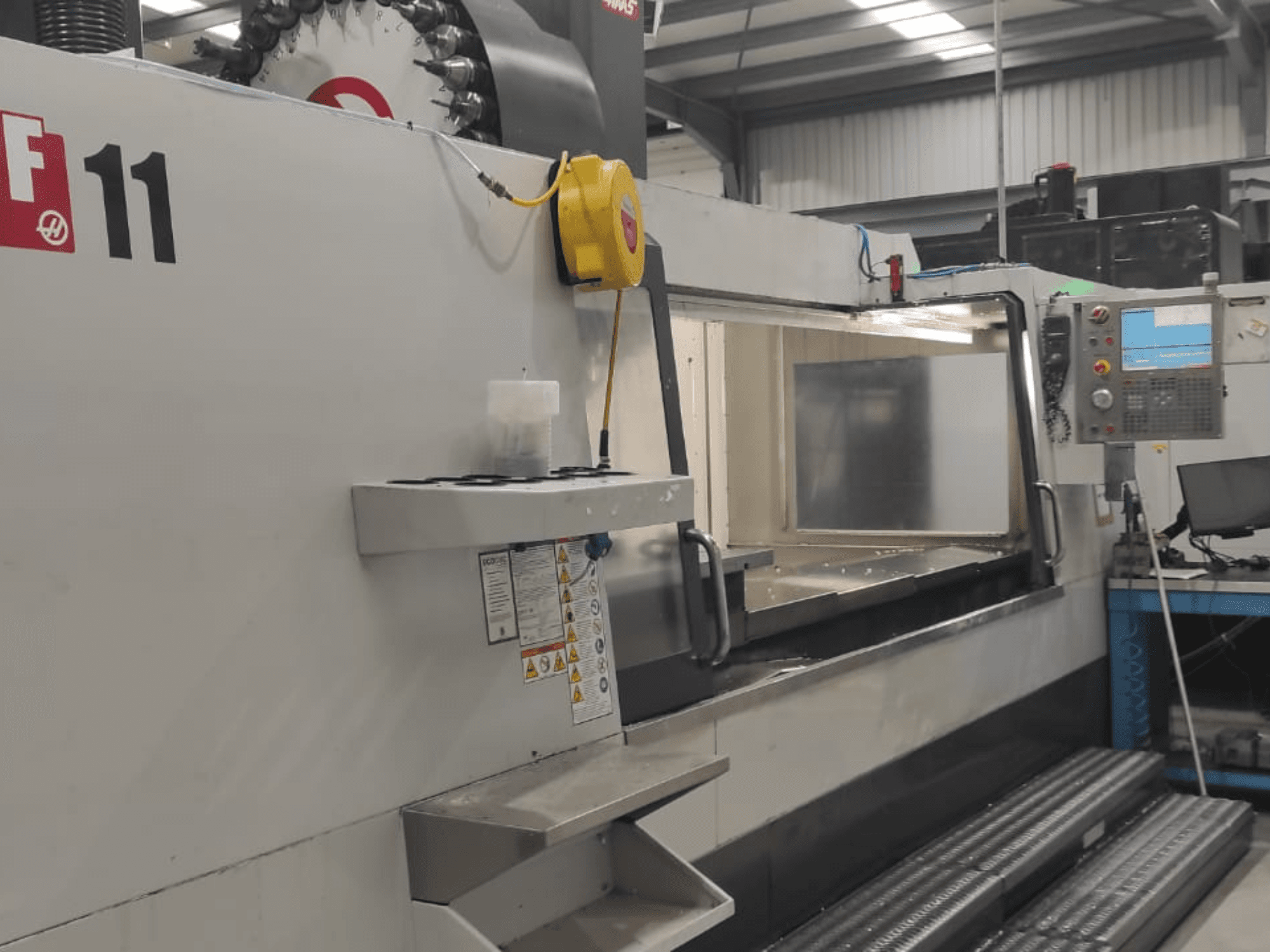 Macchinario di Haas, modello VF-11, mostrato da una vista frontale con pannello di controllo, ampia area di lavoro ed etichette di sicurezza visibili.