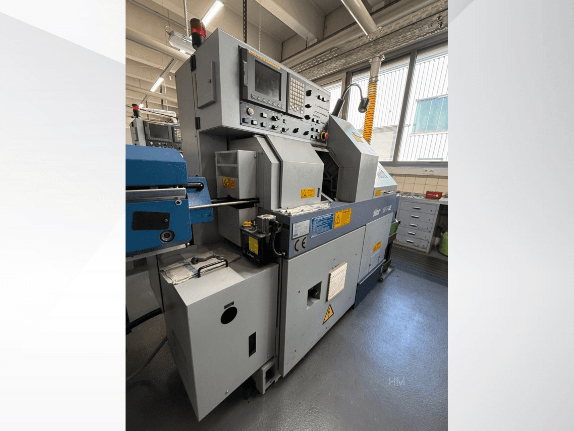 Vista frontale della macchina lithec 3231, che mostra il pannello di controllo, il motore e la sezione di alimentazione blu in un ambiente industriale ben illuminato.