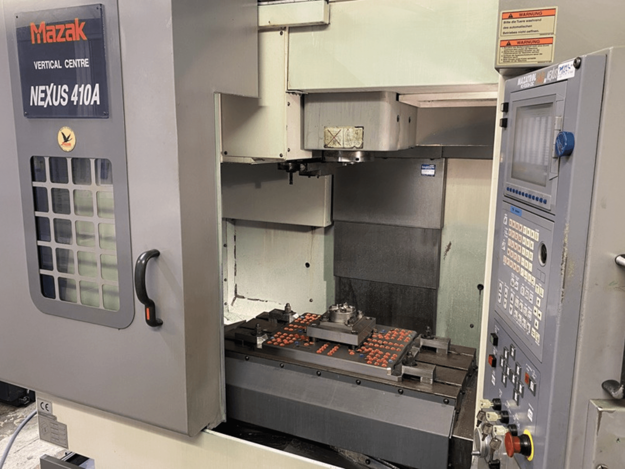 Centro di lavoro verticale Mazak VCN410, vista frontale che mostra il pannello di controllo e l'interno della macchina con il pezzo montato.