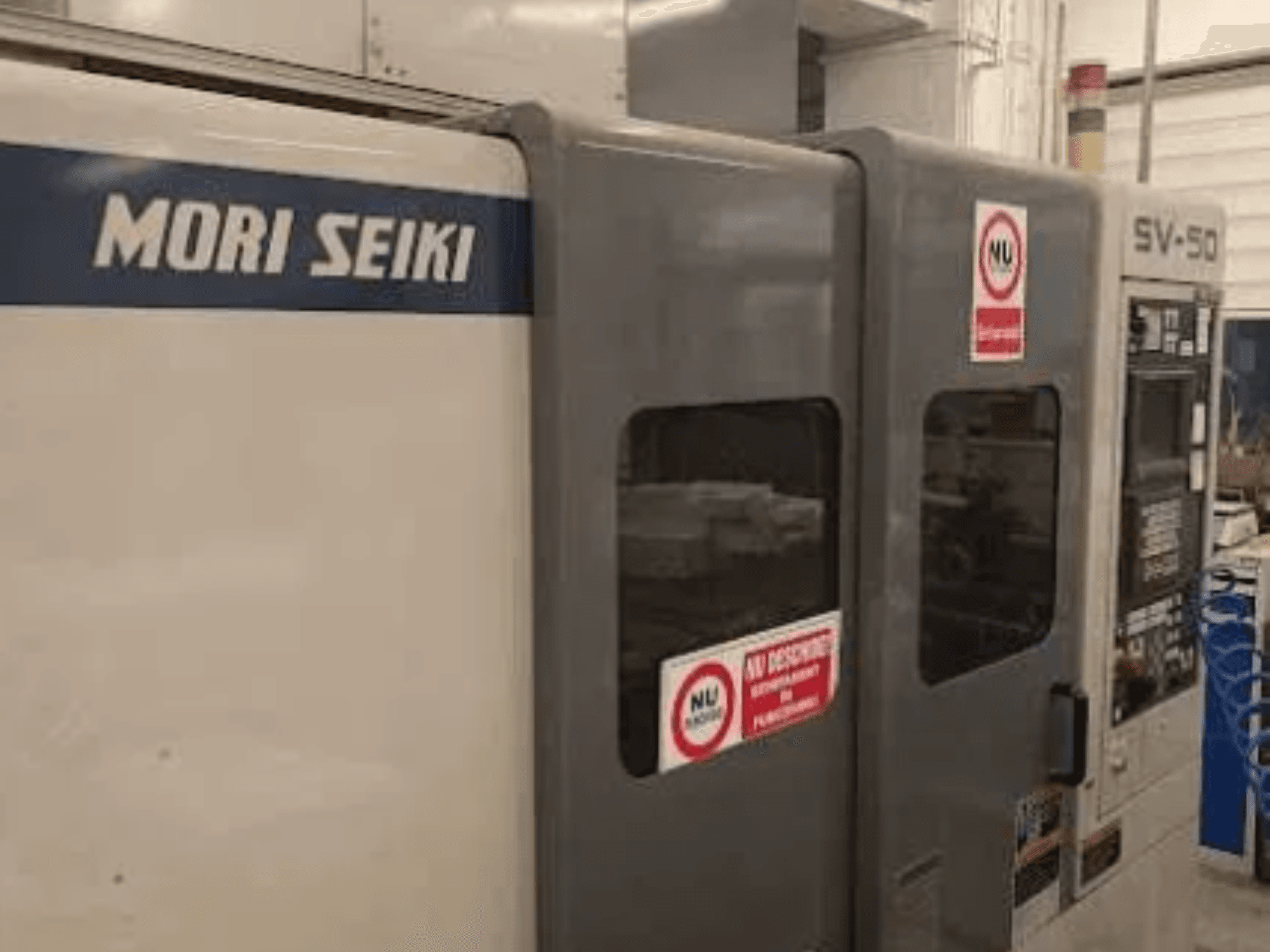 Macchina CNC MORI SEIKI SV-50, vista laterale; pannello di controllo e adesivi di sicurezza.