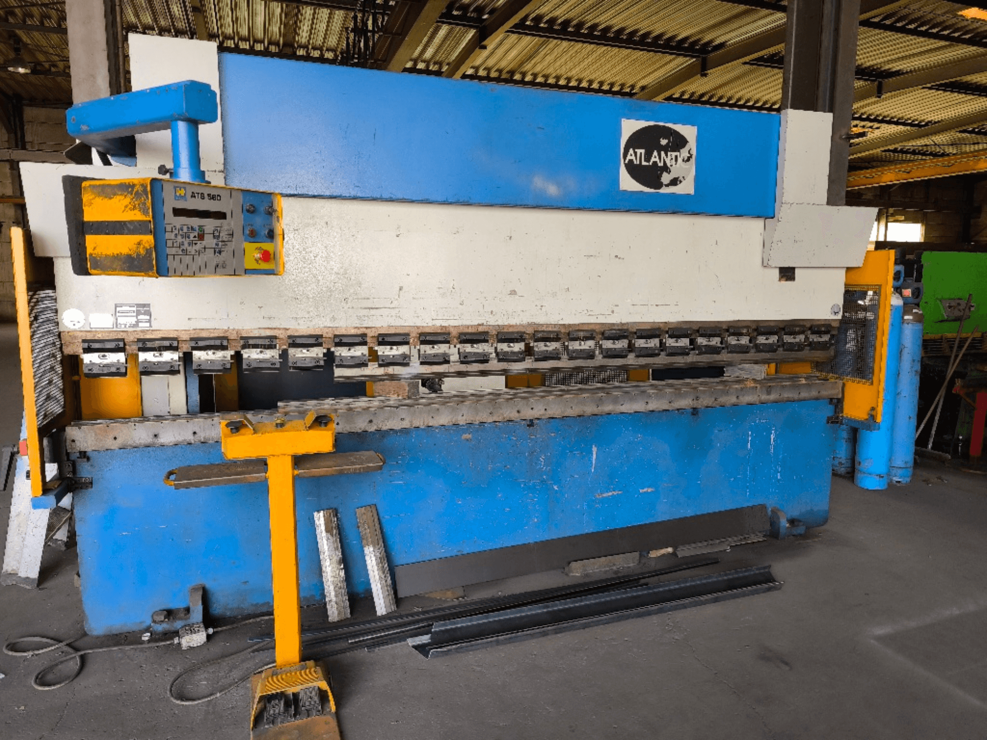 Vista frontale della pressa piegatrice ATLANTIC HPES-40-135, con pannello di controllo, utensili di piegatura e pezzi metallici accostati ad essa.