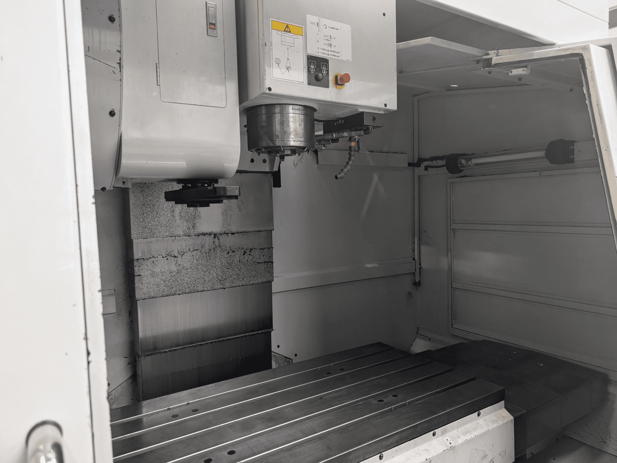Vista interna di una fresatrice CNC con un grande piano di lavoro in metallo e un motore mandrino, con i componenti dettagliati e il pannello di controllo.