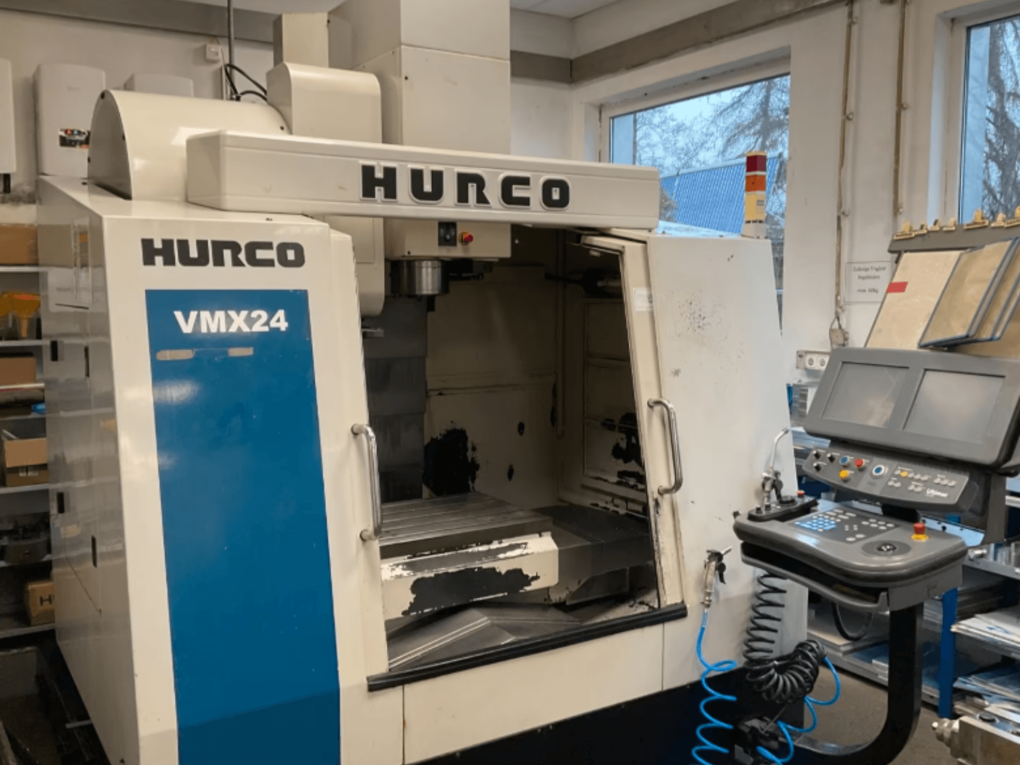 Centro di lavoro verticale Hurco VMX24 visto frontalmente, con in evidenza il pannello di controllo, la testa del mandrino e l'area di lavoro; sono visibili alcuni segni di usura.