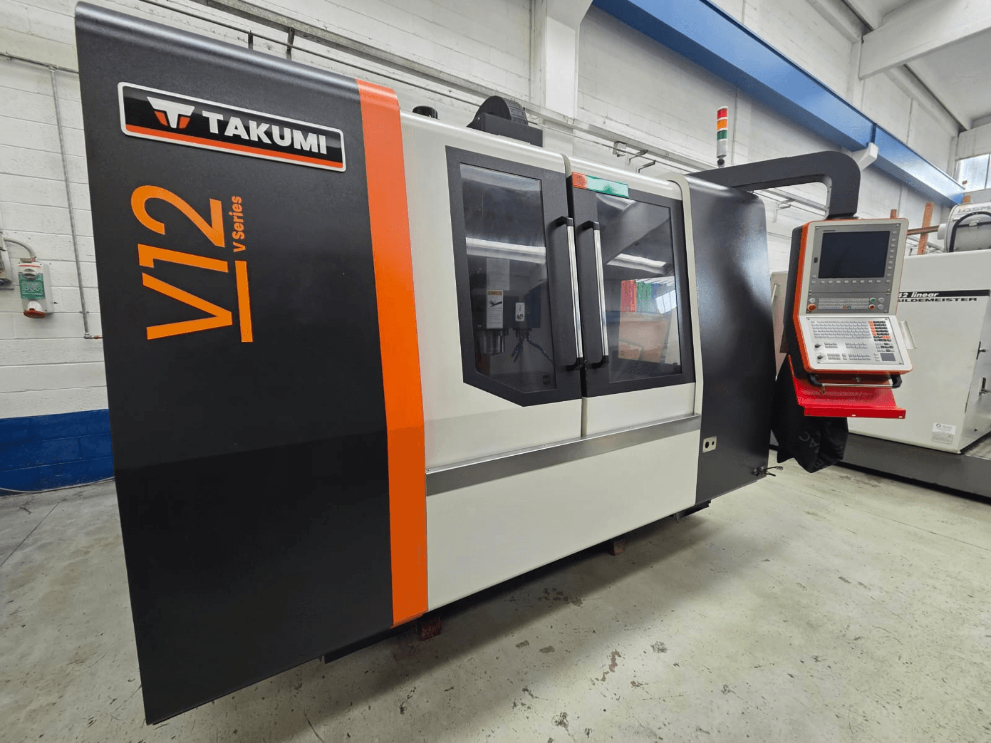 La fresatrice CNC Takumi serie V12 V, vista frontale, presenta un pannello di controllo e ampie finestre in vetro.