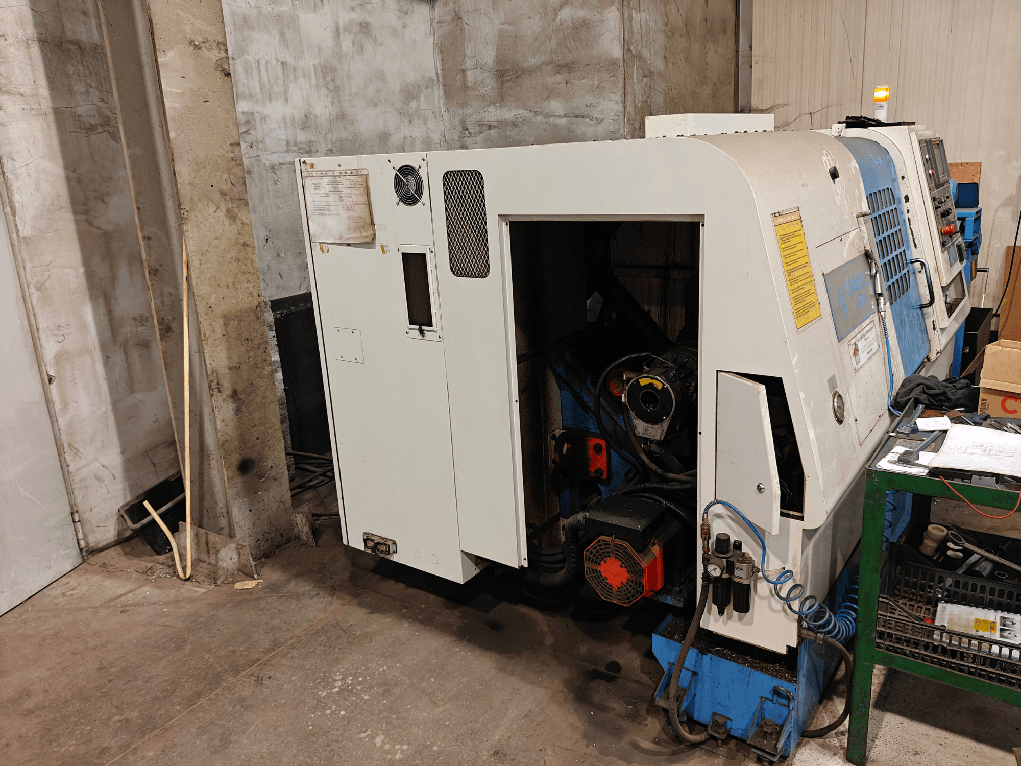 Vista frontale di un tornio, marca e modello non specificati, con comandi e componenti del motore visibili.