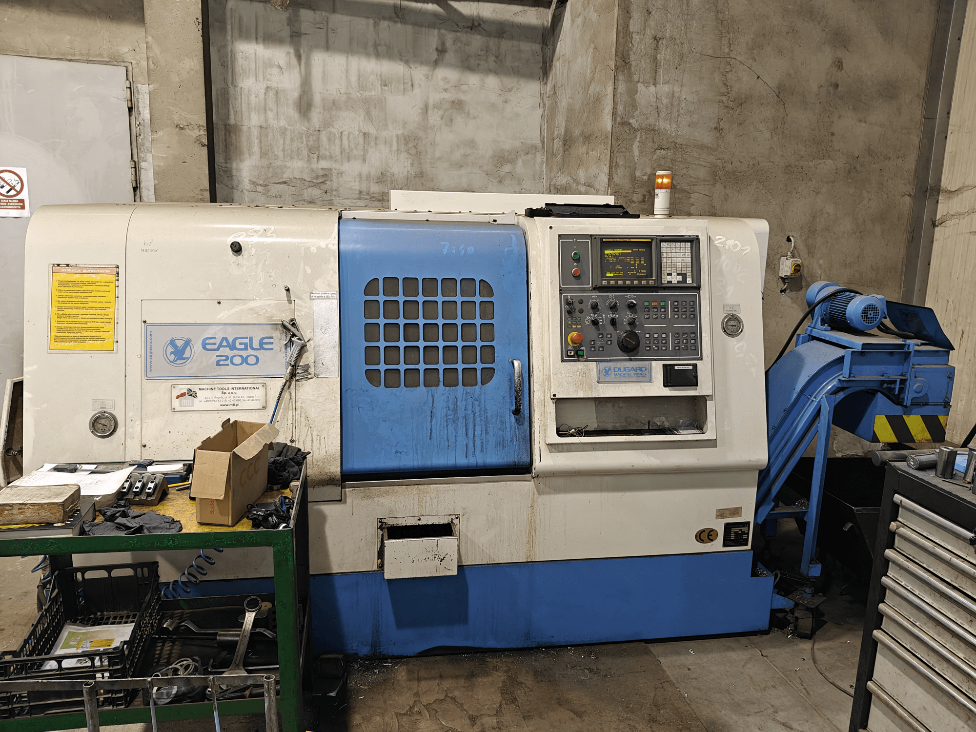 Macchina CNC Eagle 200, vista frontale con pannello di controllo, vari utensili su un carrello verde. Usura visibile e luci di funzionamento.