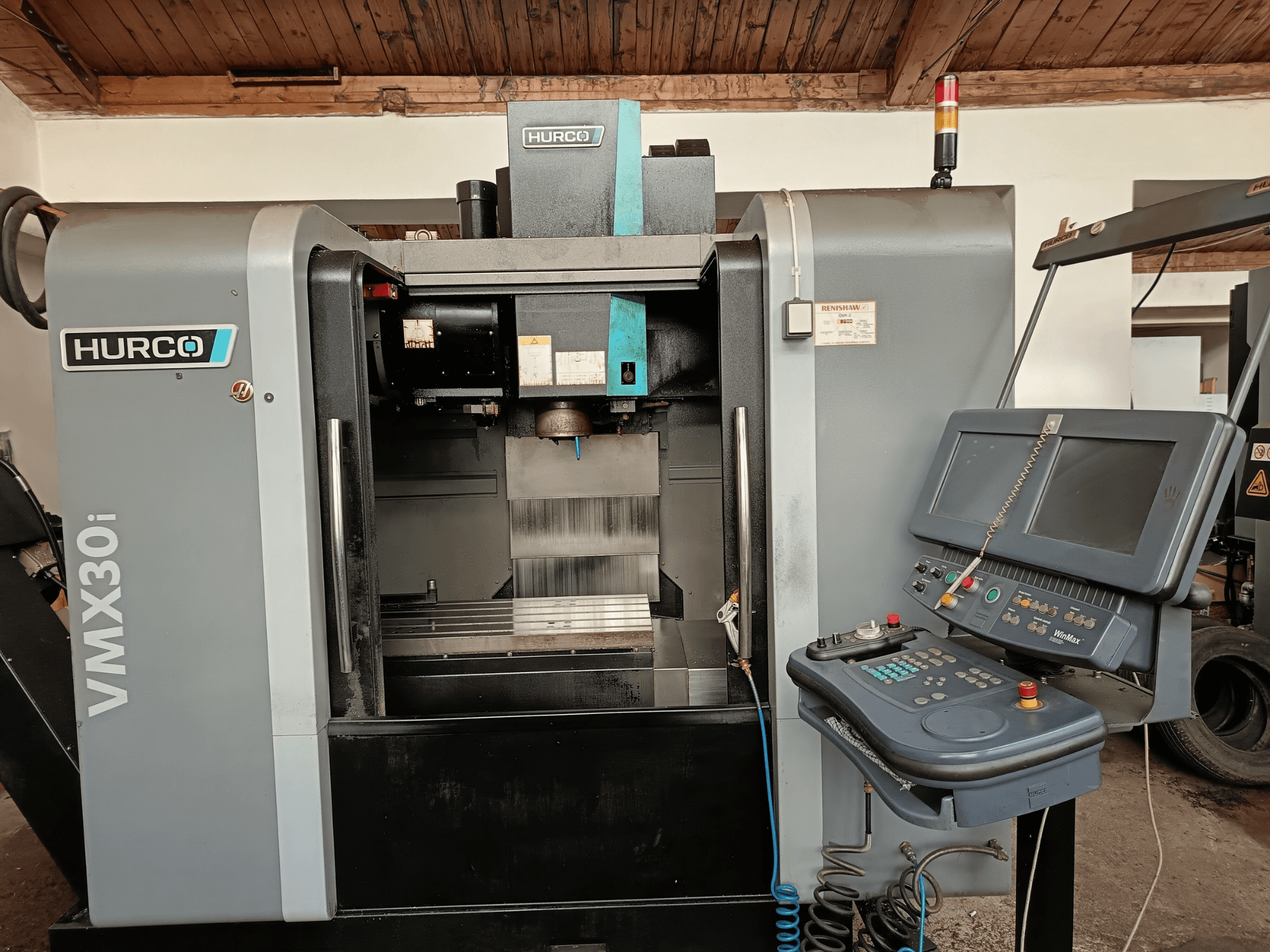 Centro di lavoro HURCO VMX30i in vista frontale, con pannello di controllo con pulsanti e monitor, area di lavoro metallica e spia luminosa.