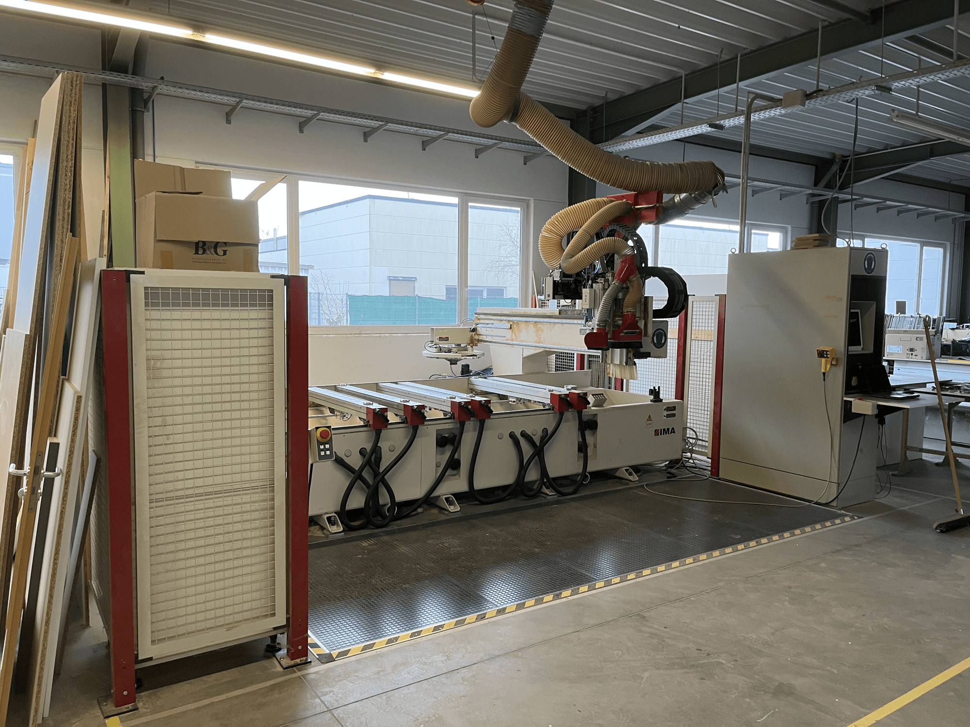 Centro di lavorazione del legno a CNC IMA BIMA 410 in officina, vista laterale con pannello di controllo e sistema di aspirazione delle polveri visibili.