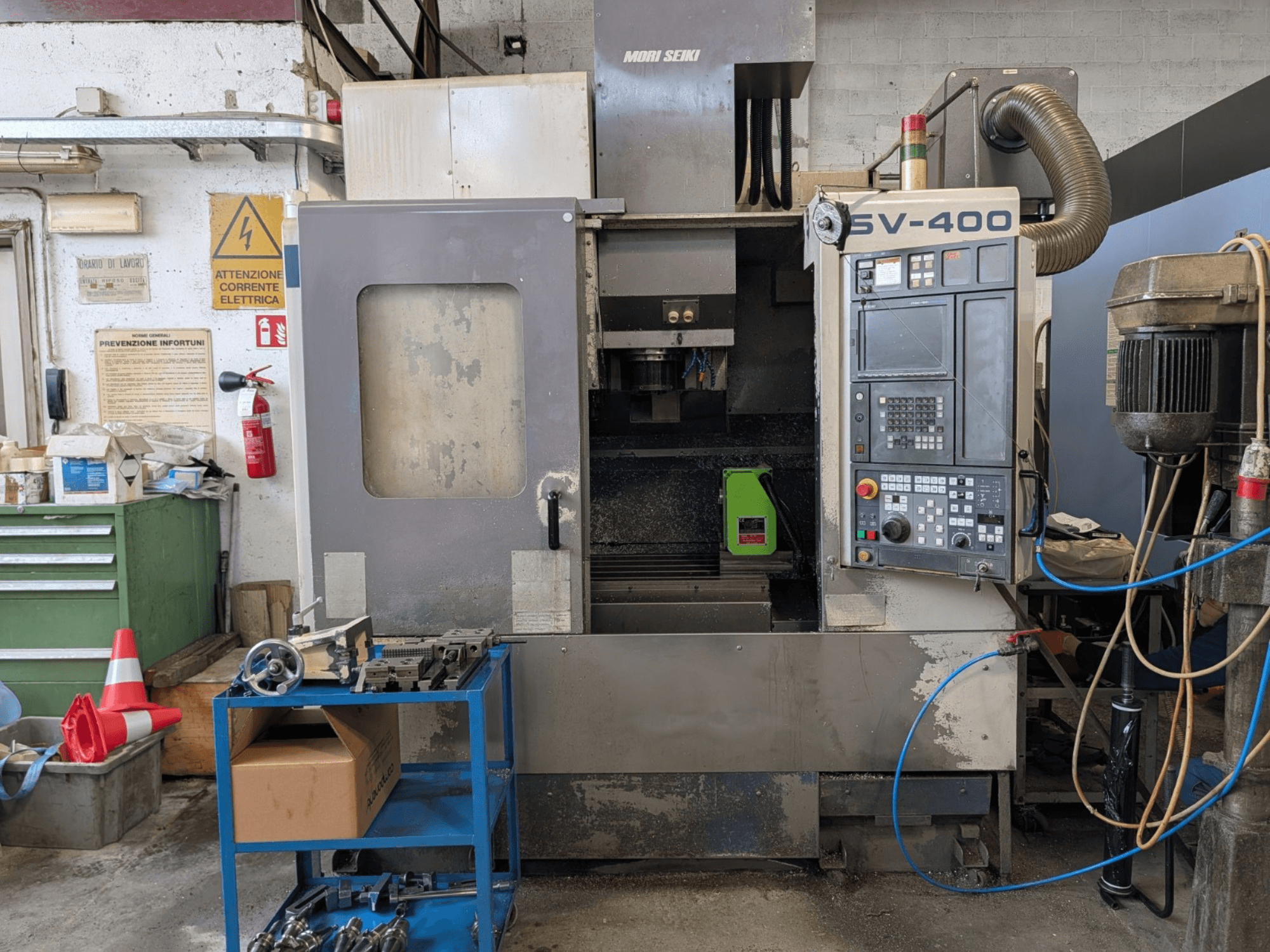 Centro di lavoro verticale MORI SEIKI SV-400 in un'officina, vista laterale, con pannello di controllo e macchine utensili vicine.