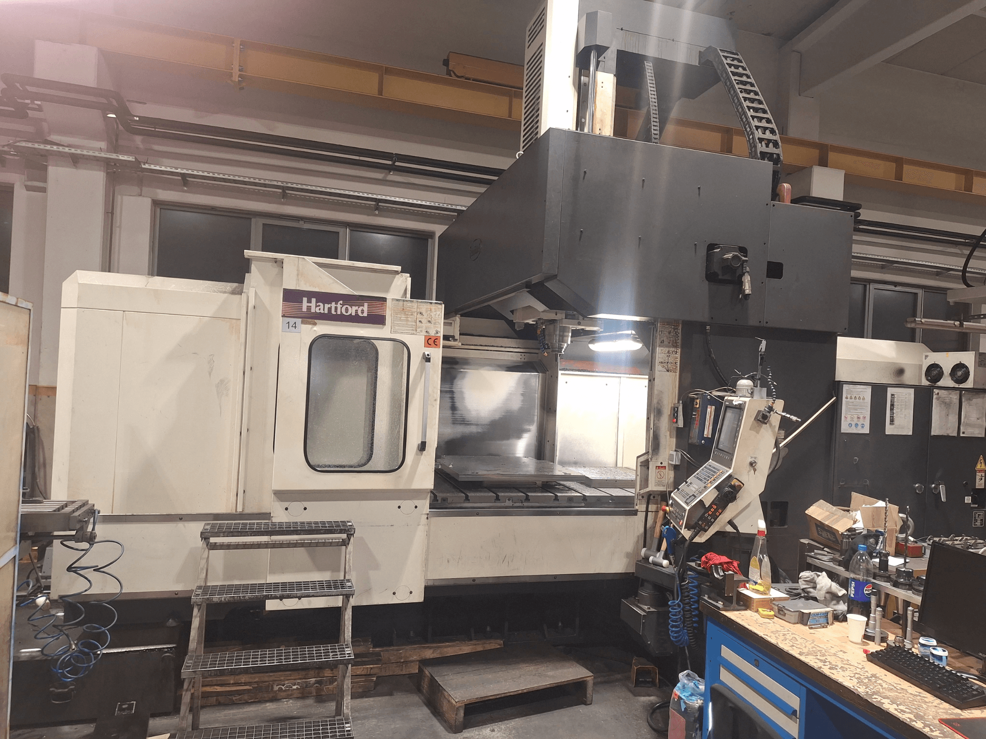 Macchina CNC Hartford, vista frontale, con comandi tecnici, gradini di accesso e area del tavolo di lavoro, in un'officina.