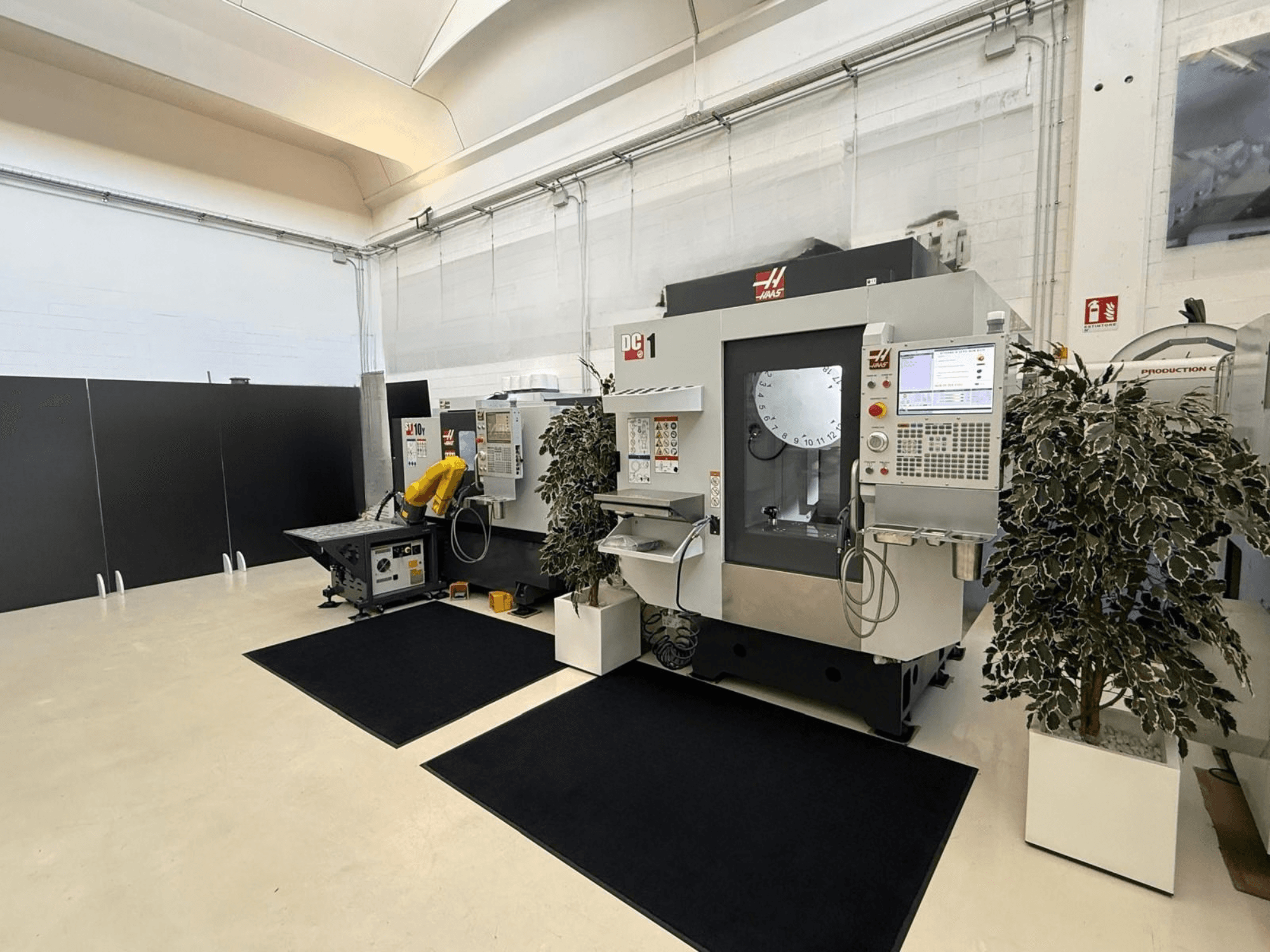 Vista frontale di un centro di lavorazione verticale HAAS DC-1 in un ambiente di lavoro pulito, con pannello di controllo touchscreen e impianti circostanti.