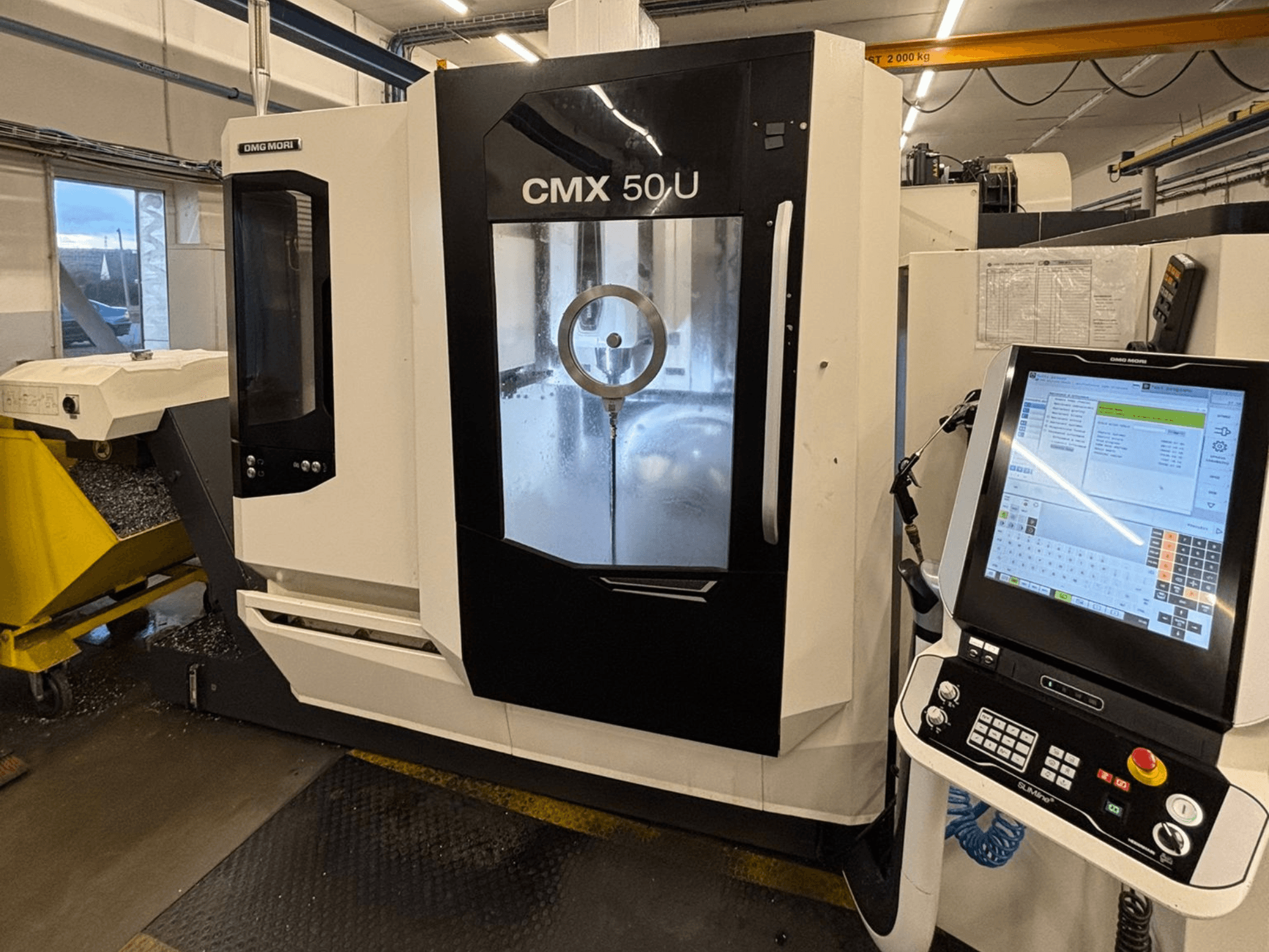 Centro di lavoro verticale DMG MORI CMX 50 U, vista frontale con pannello di controllo e display in vetro, che mostra la meccanica interna.