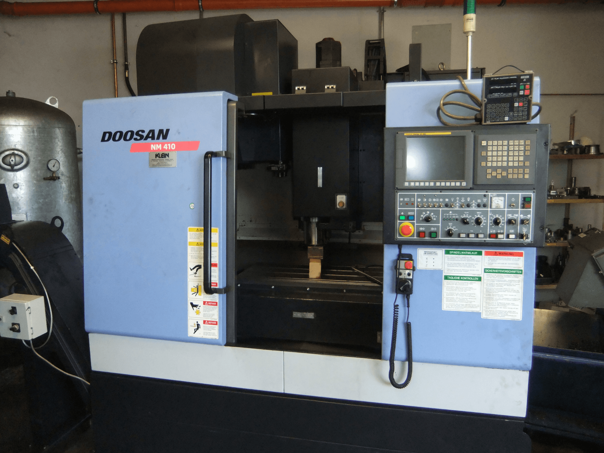 Centro di lavorazione verticale DOOSAN NM 410, vista frontale, con pannello di controllo, zona mandrino ed etichette di sicurezza.