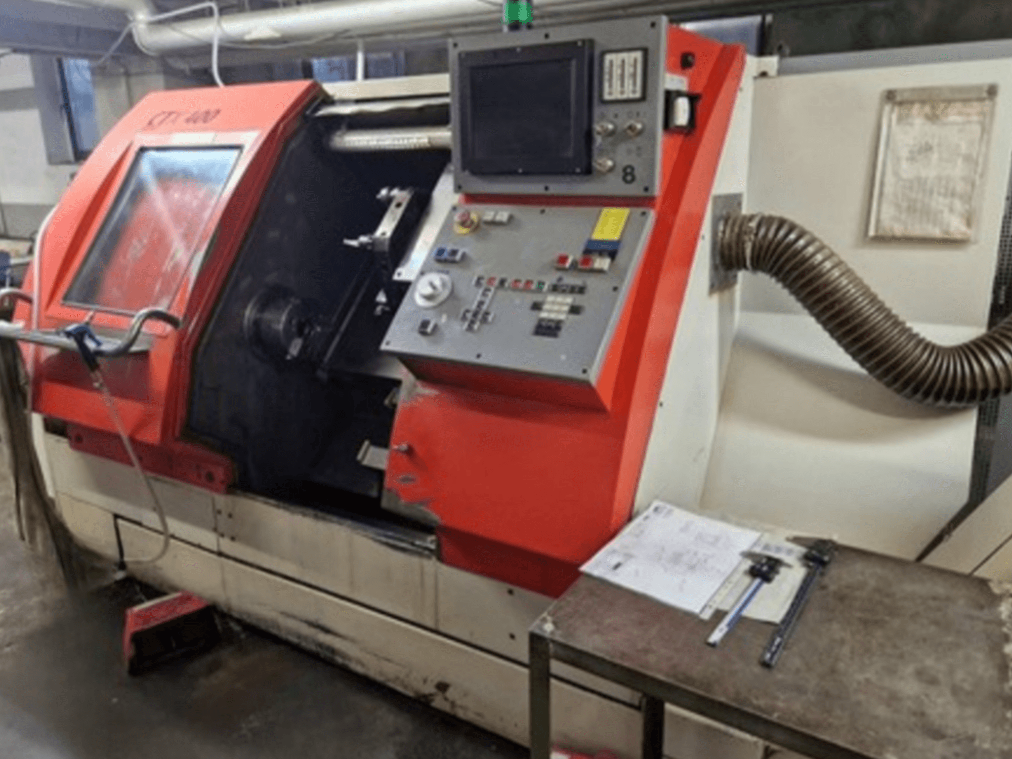 Tornio orizzontale Gildemeister CTX 400 in vista frontale, con pannello di controllo, porta aperta e tavolo da officina con utensili.