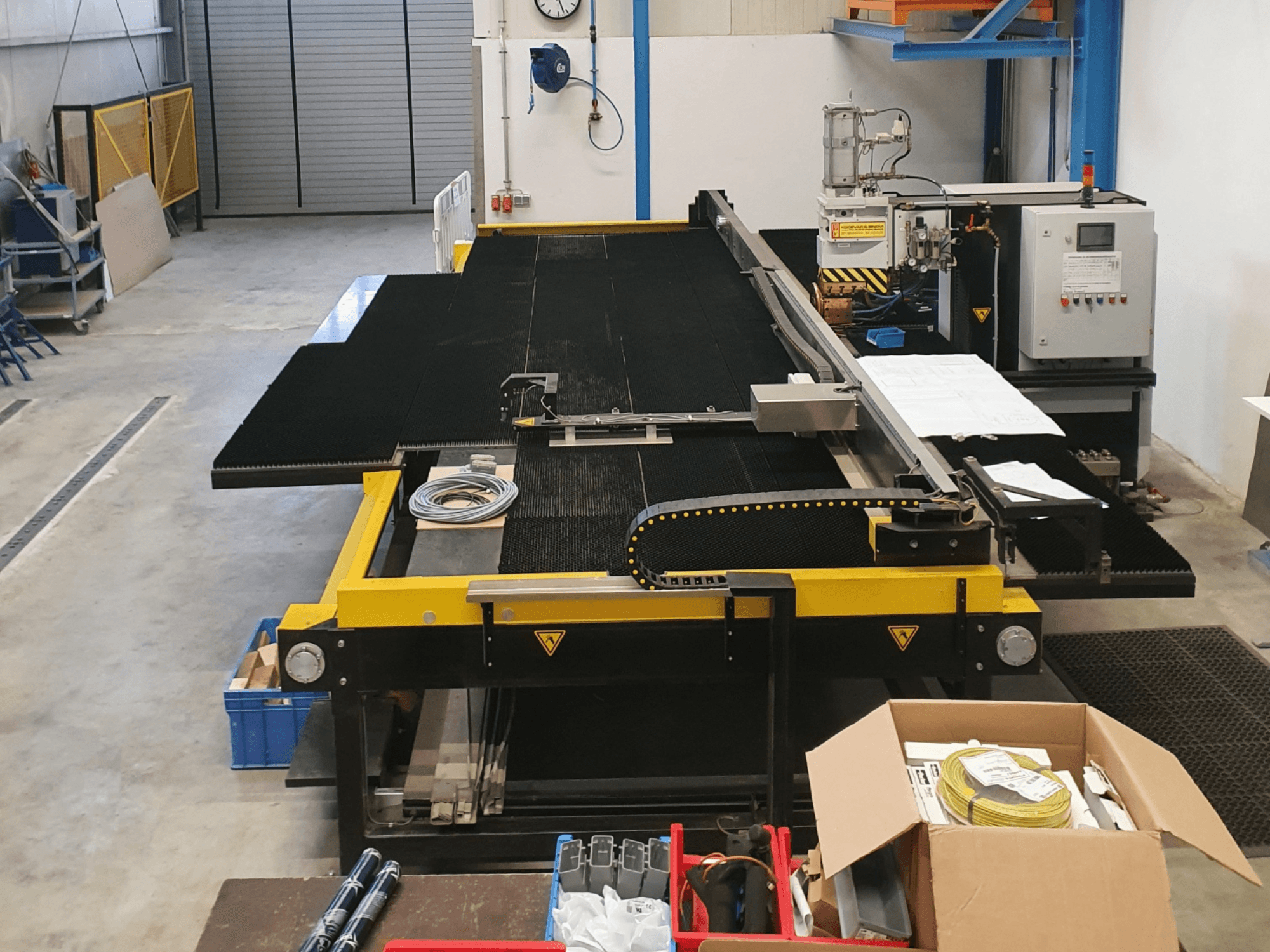 Macchina da taglio industriale con caratteristiche gialle e nere, vista frontale, che mostra comandi e accessori in un ambiente di fabbrica.