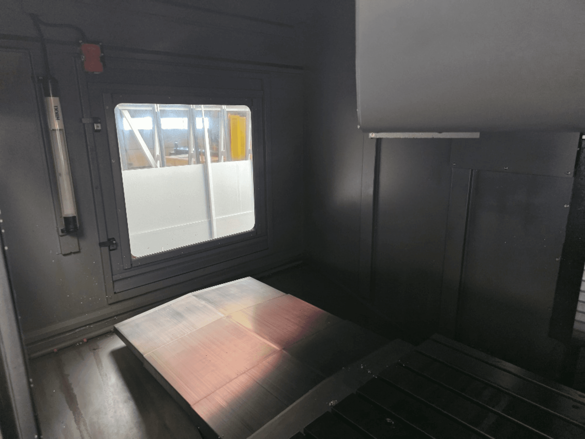 Vista interna di un involucro di macchina con una piastra metallica lucida, una finestra laterale e un'illuminazione minima. Nessun marchio visibile.